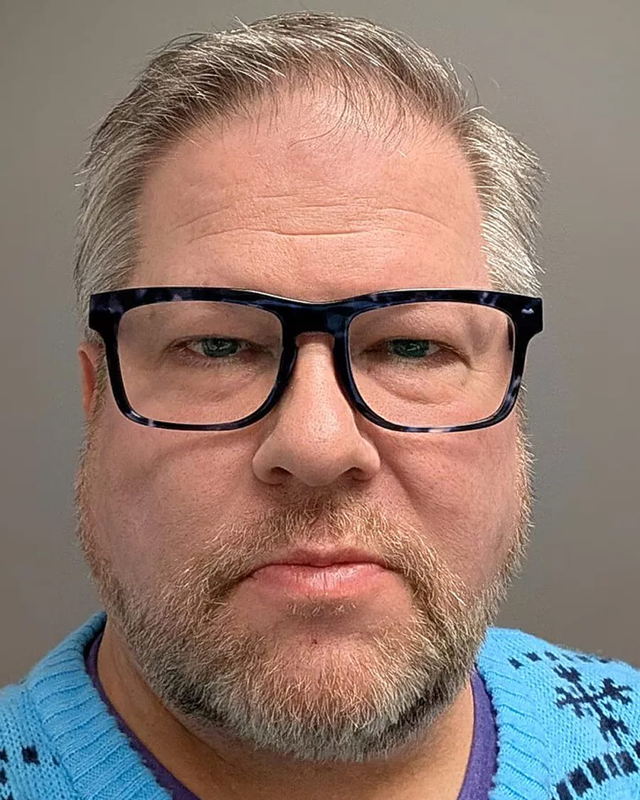 Man with glasses and beard wearing a blue sweater.
