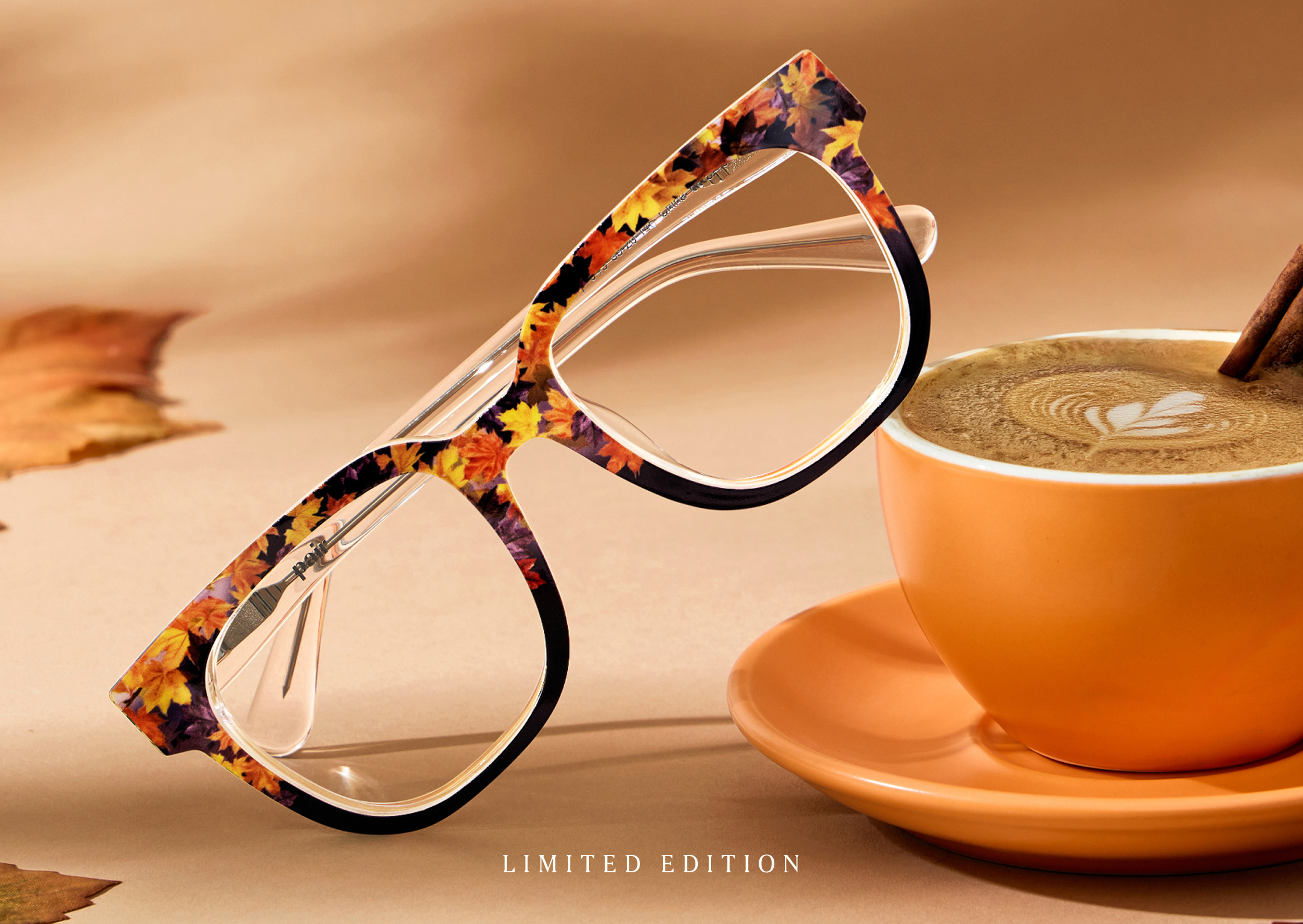 Eyeglasses with autumn leaf pattern and an orange coffee cup.