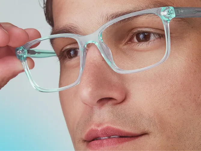 A close-up of a man holding the side of his light blue translucent eyeglasses.