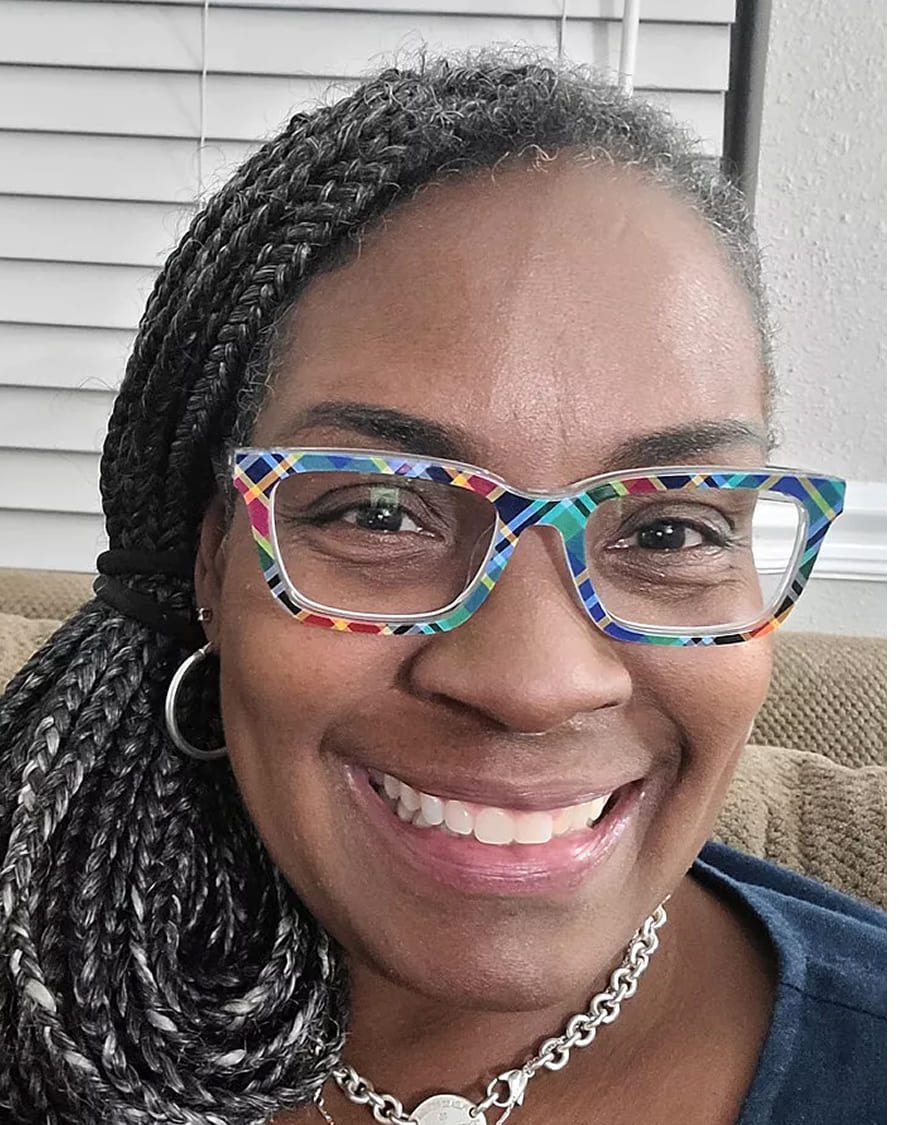 Person smiling, wearing colorful glasses and braided hair.