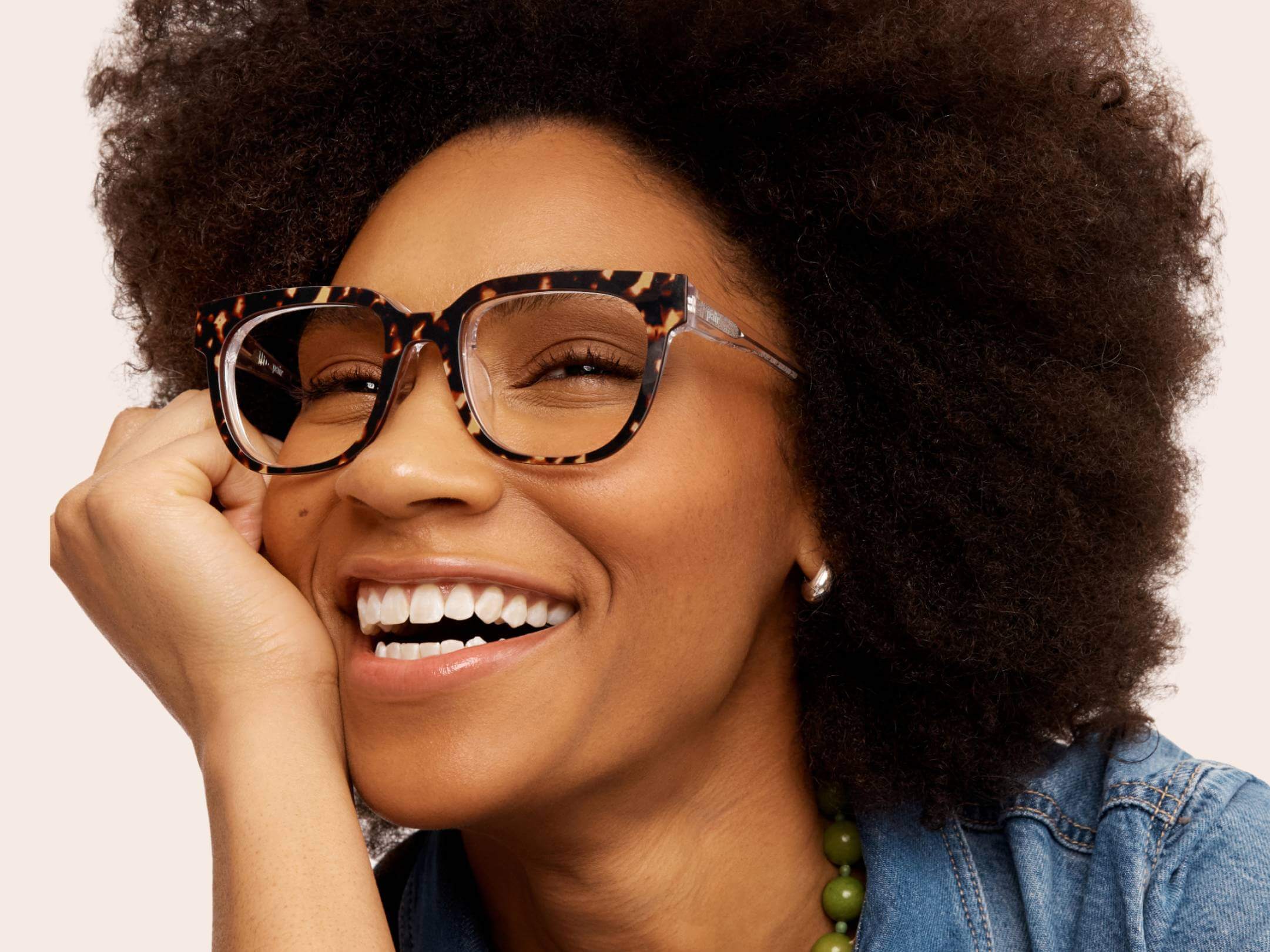 Smiling person wearing tortoiseshell glasses and a denim jacket.
