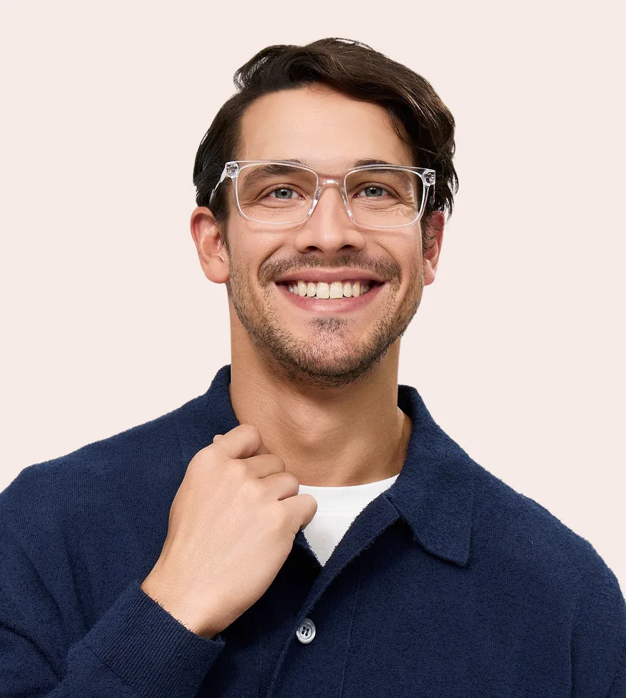 A smiling man with brown hair and light stubble wearing clear-framed glasses and a blue collared shirt.