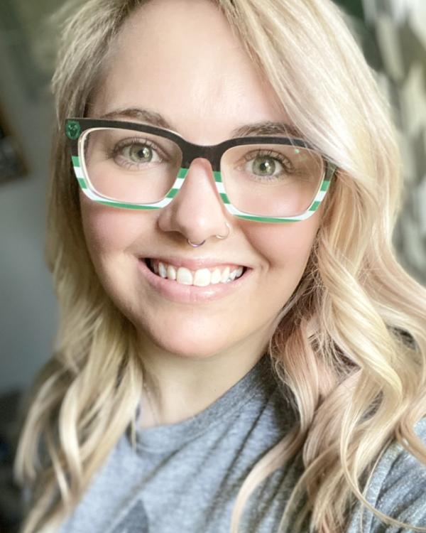 Person with glasses smiling, wearing a gray shirt.