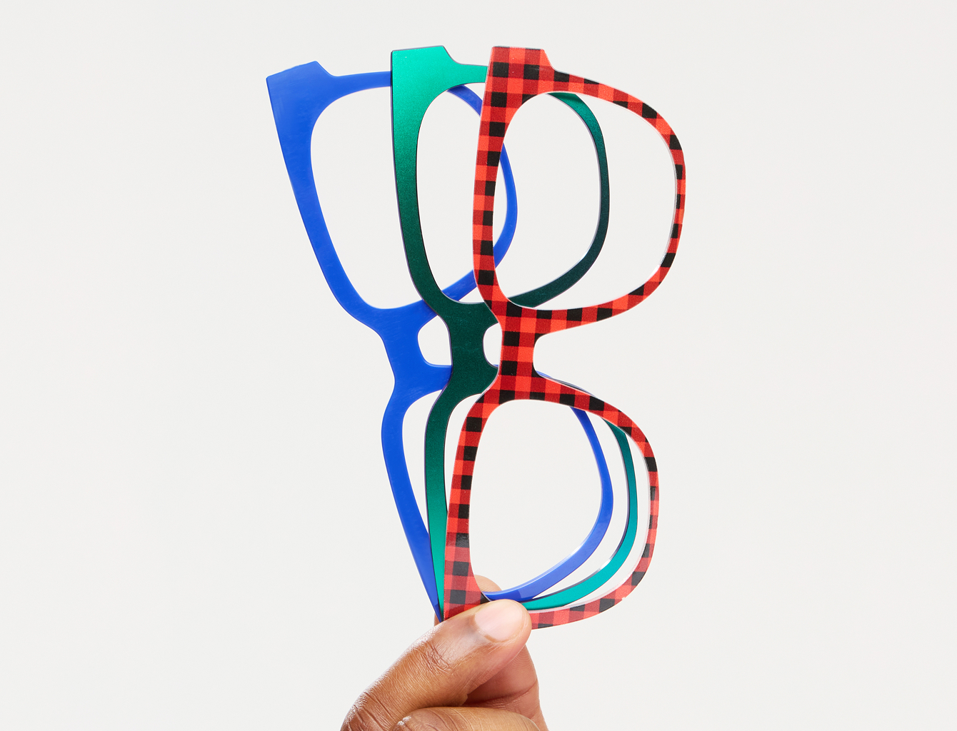 Hand holding three colorful eyeglass frames against a white background.