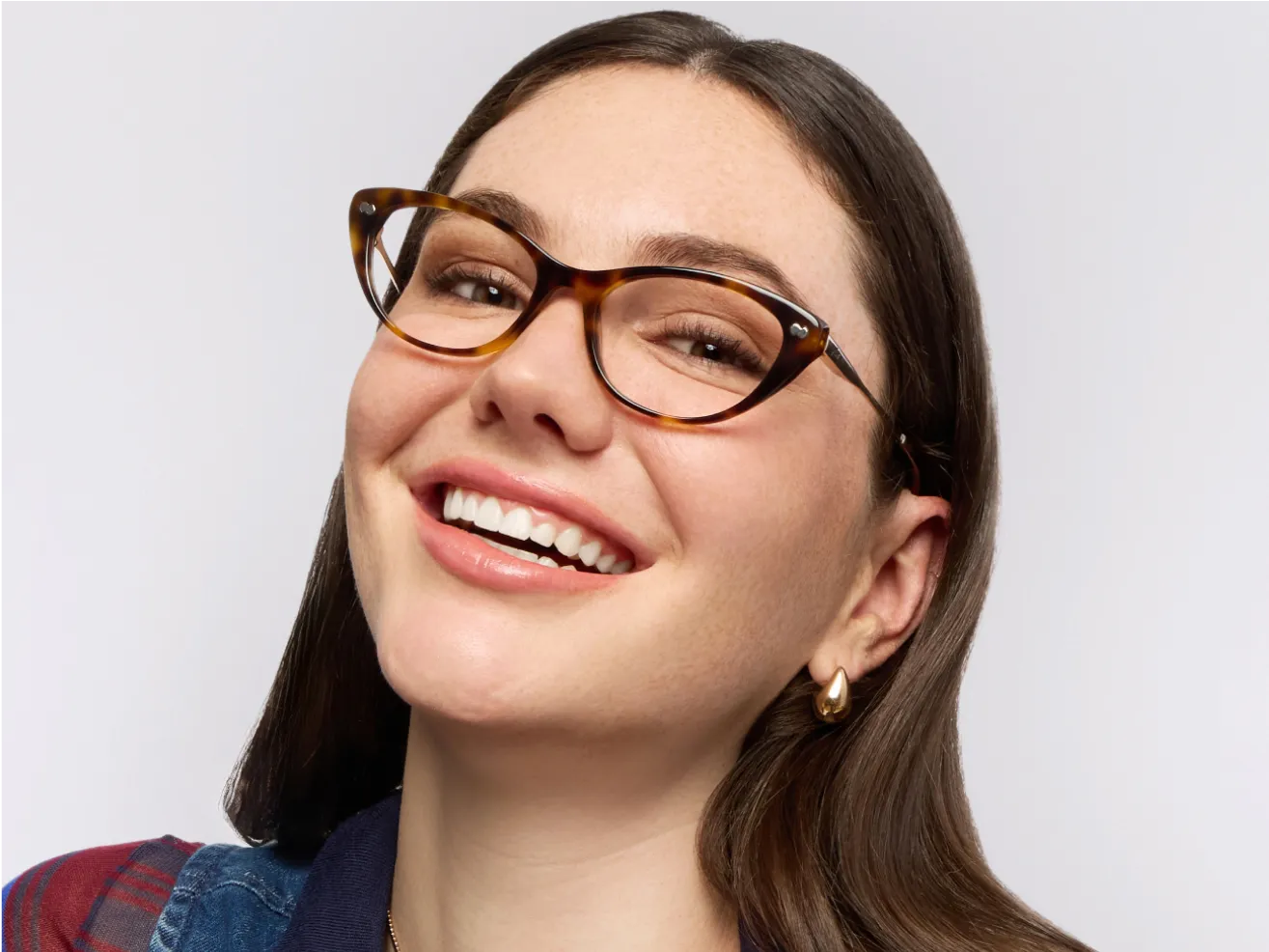 Smiling person wearing glasses with tortoiseshell frames against a neutral background.