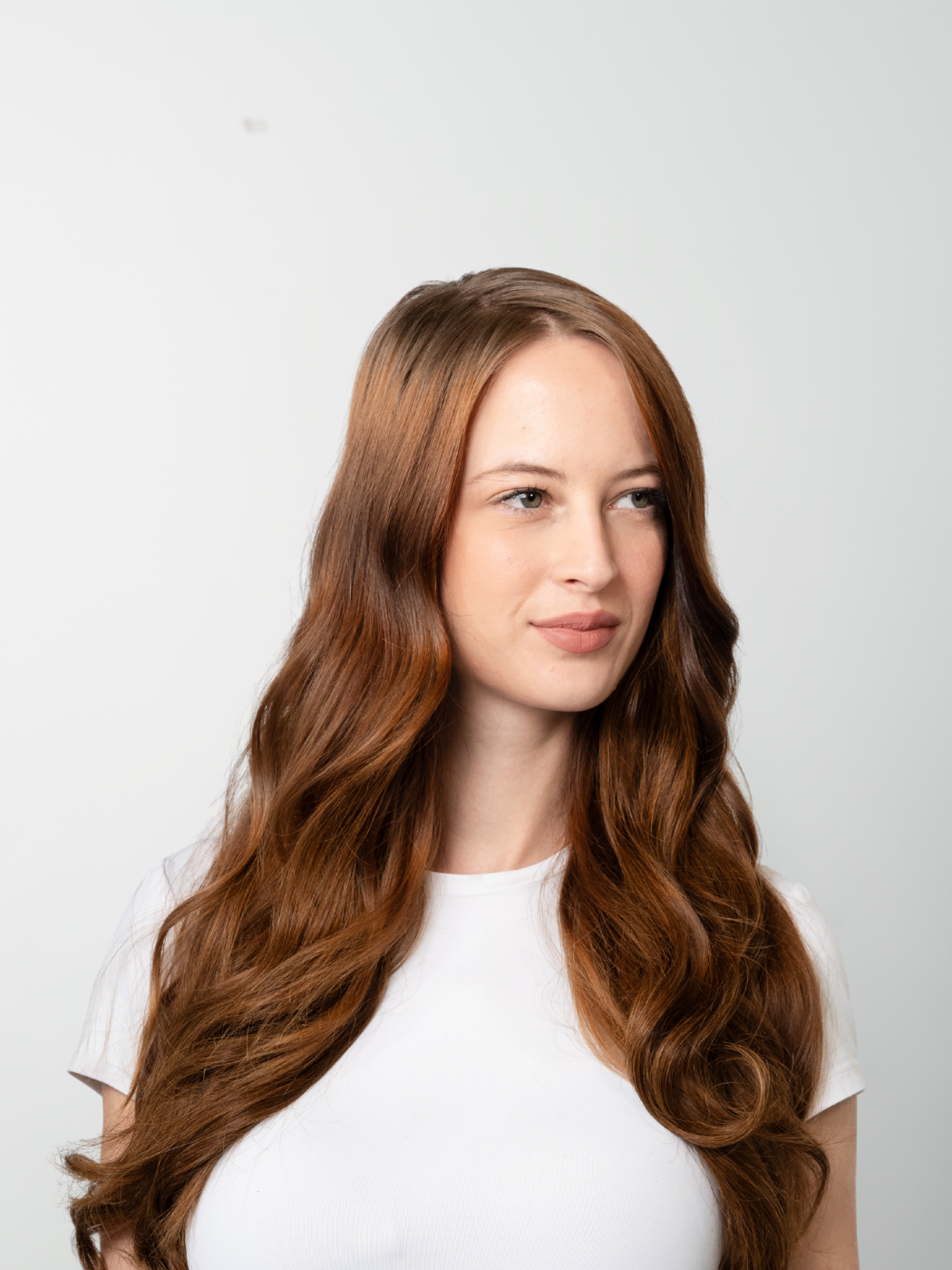 Model with long wavy auburn hair parted in the middle, wearing a white t-shirt.