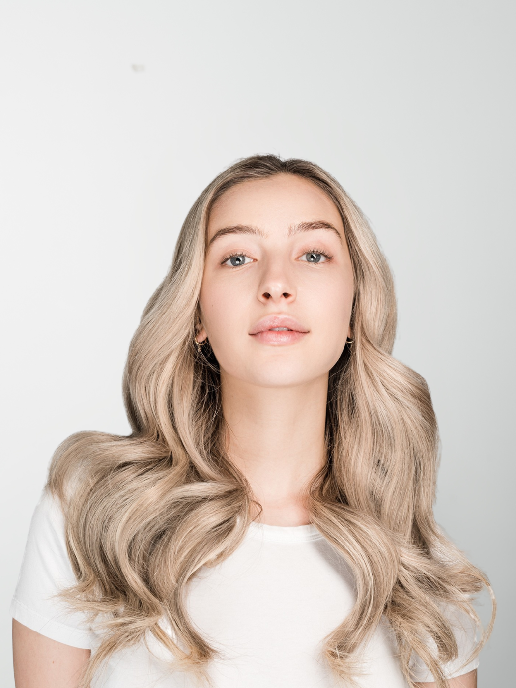 Model with long voluminous blonde hair and loose waves looking directly at the camera.