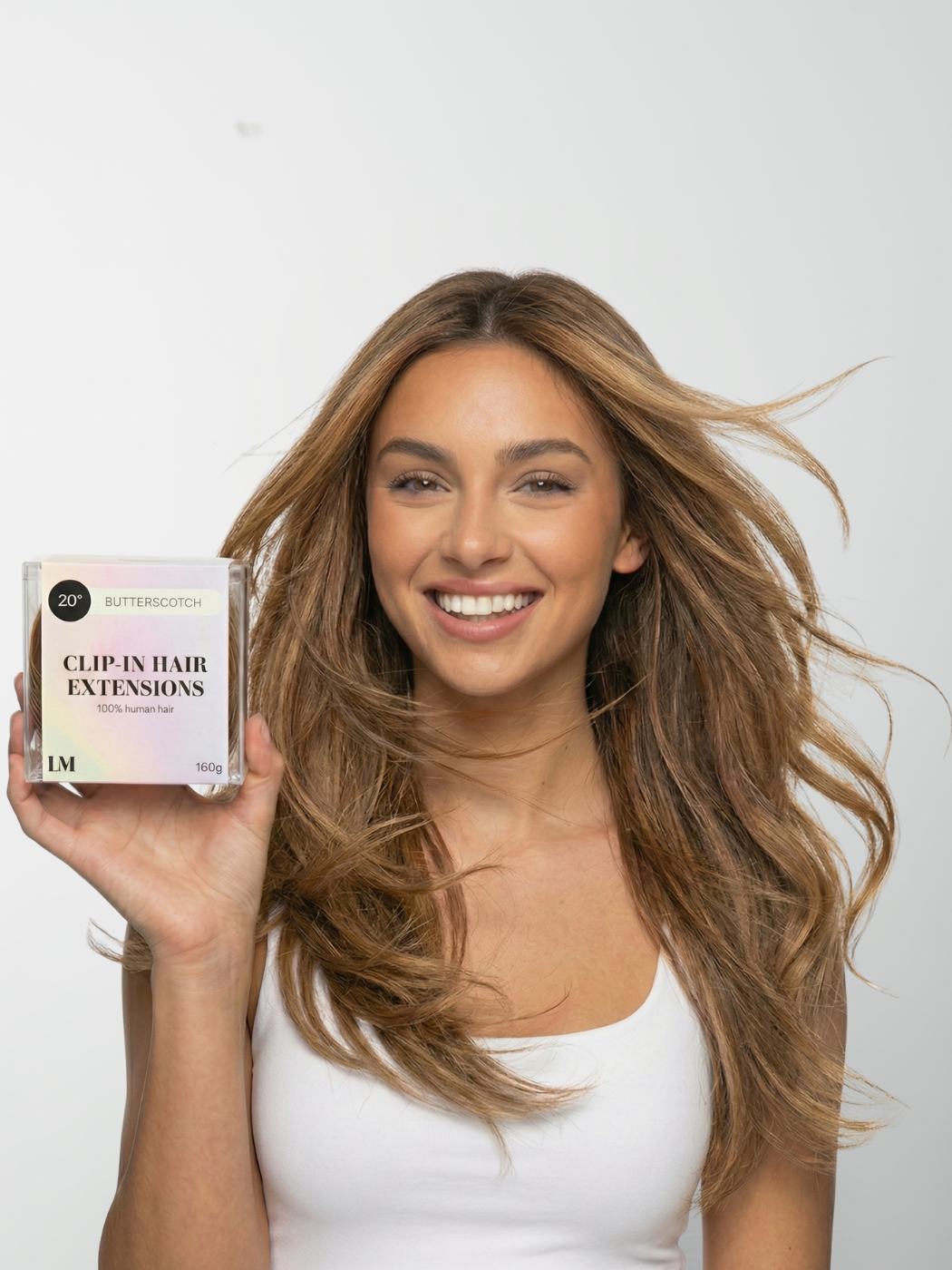 A smiling woman with long, wavy hair holds a box of Butterscotch clip-in hair extensions.