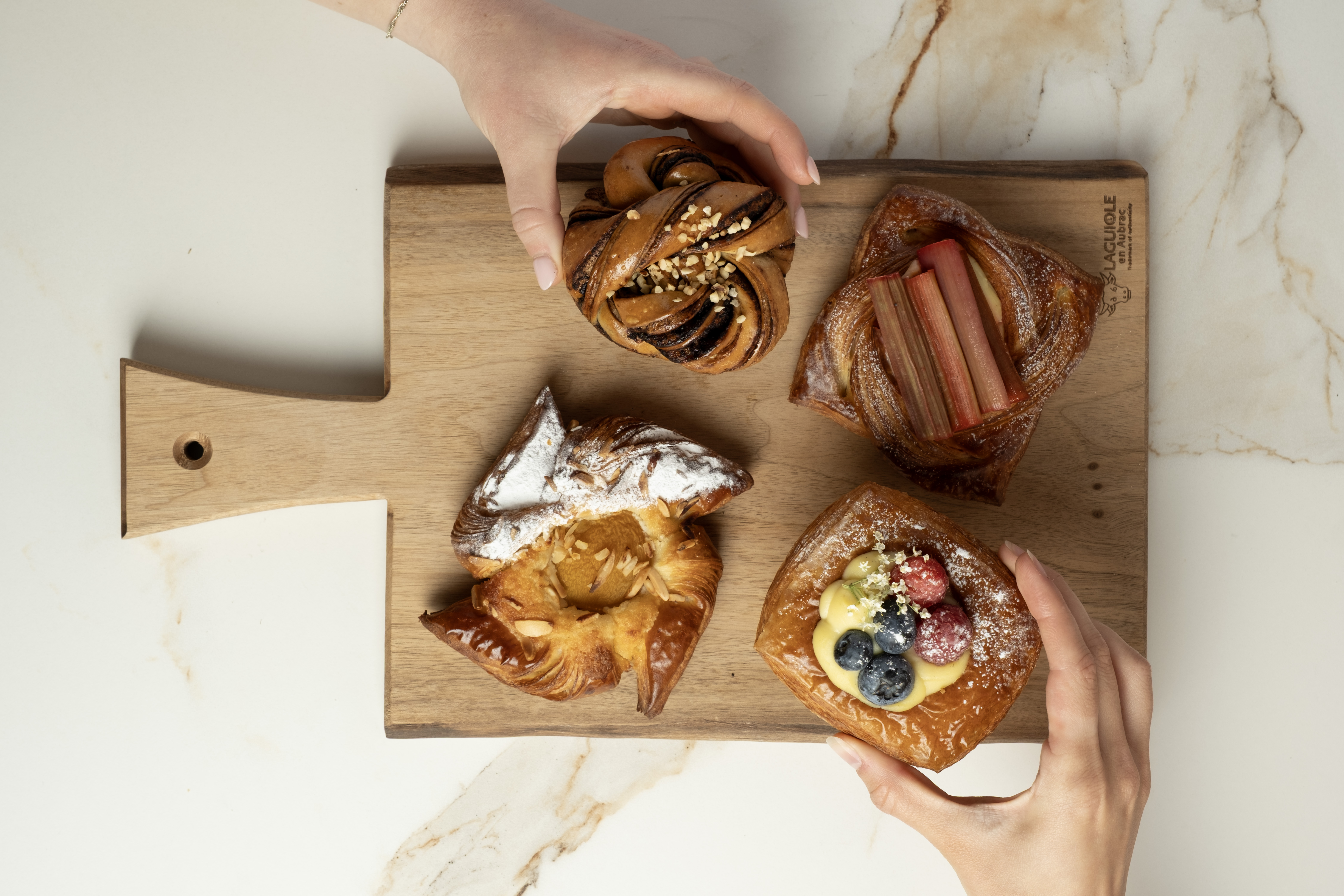 Hands reaching for assorted pastries on a wooden board.
