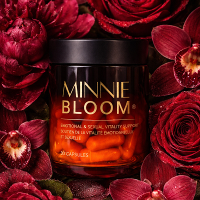 A jar of Minnie Bloom capsules with a black lid, nestled amongst dewy, deep red flowers.
