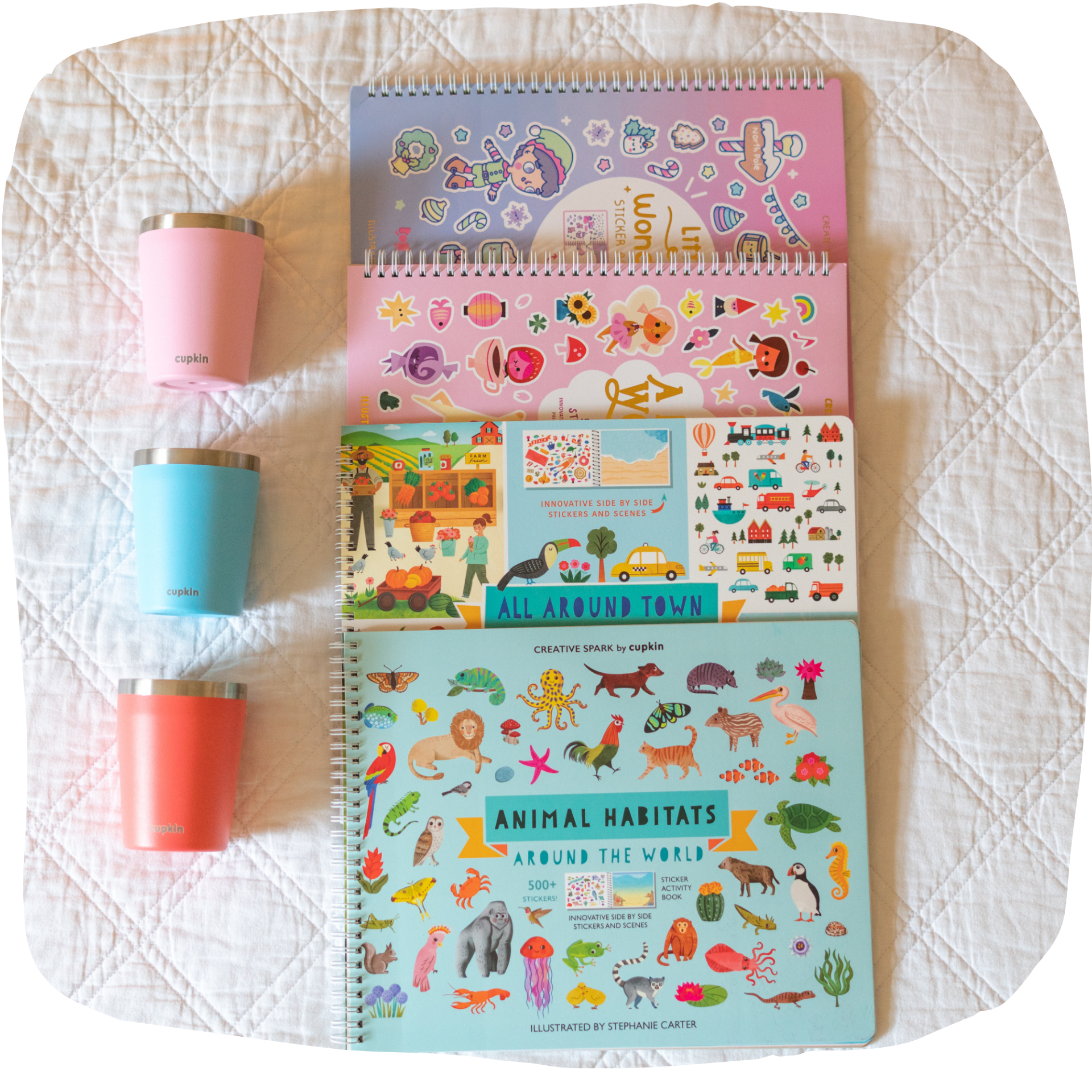 Three colorful cups and four sticker books on a quilted surface.