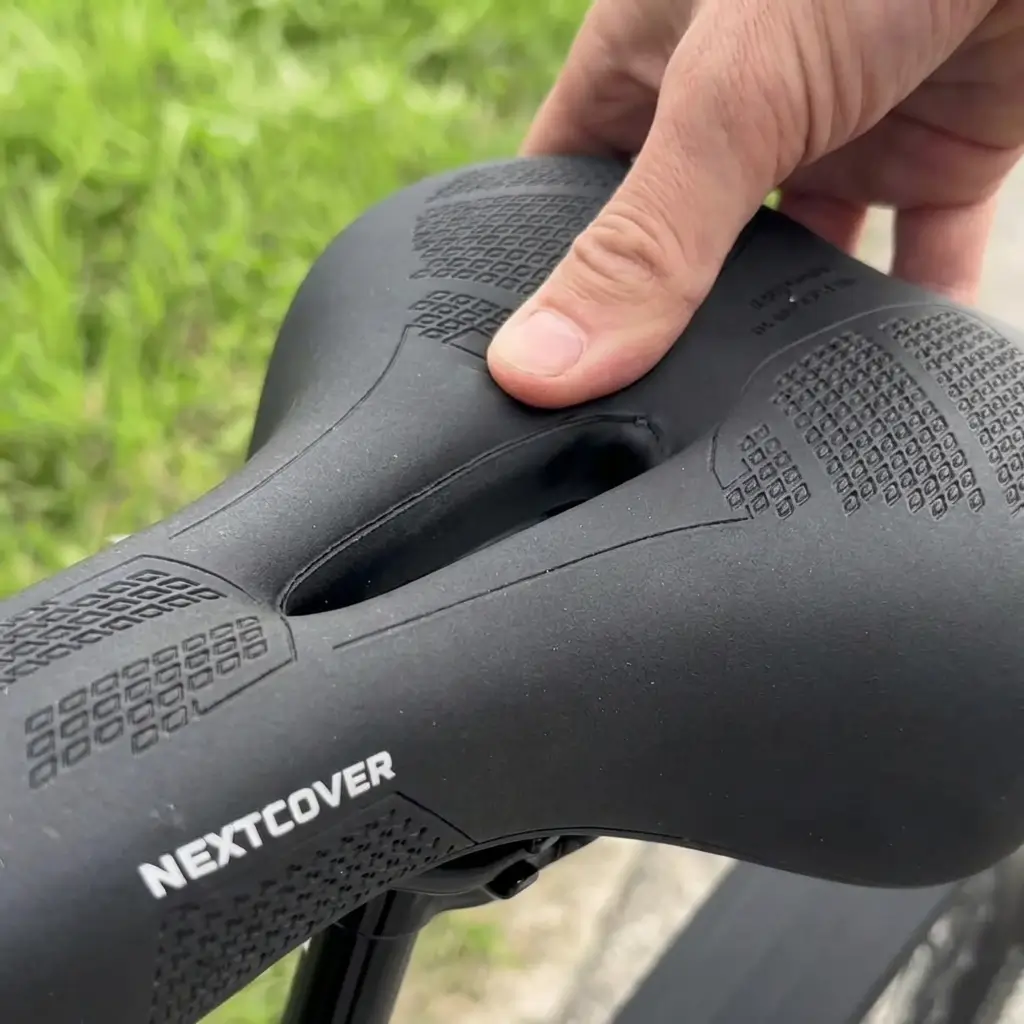 A close-up of a hand pressing down on a black padded bicycle saddle outdoors.