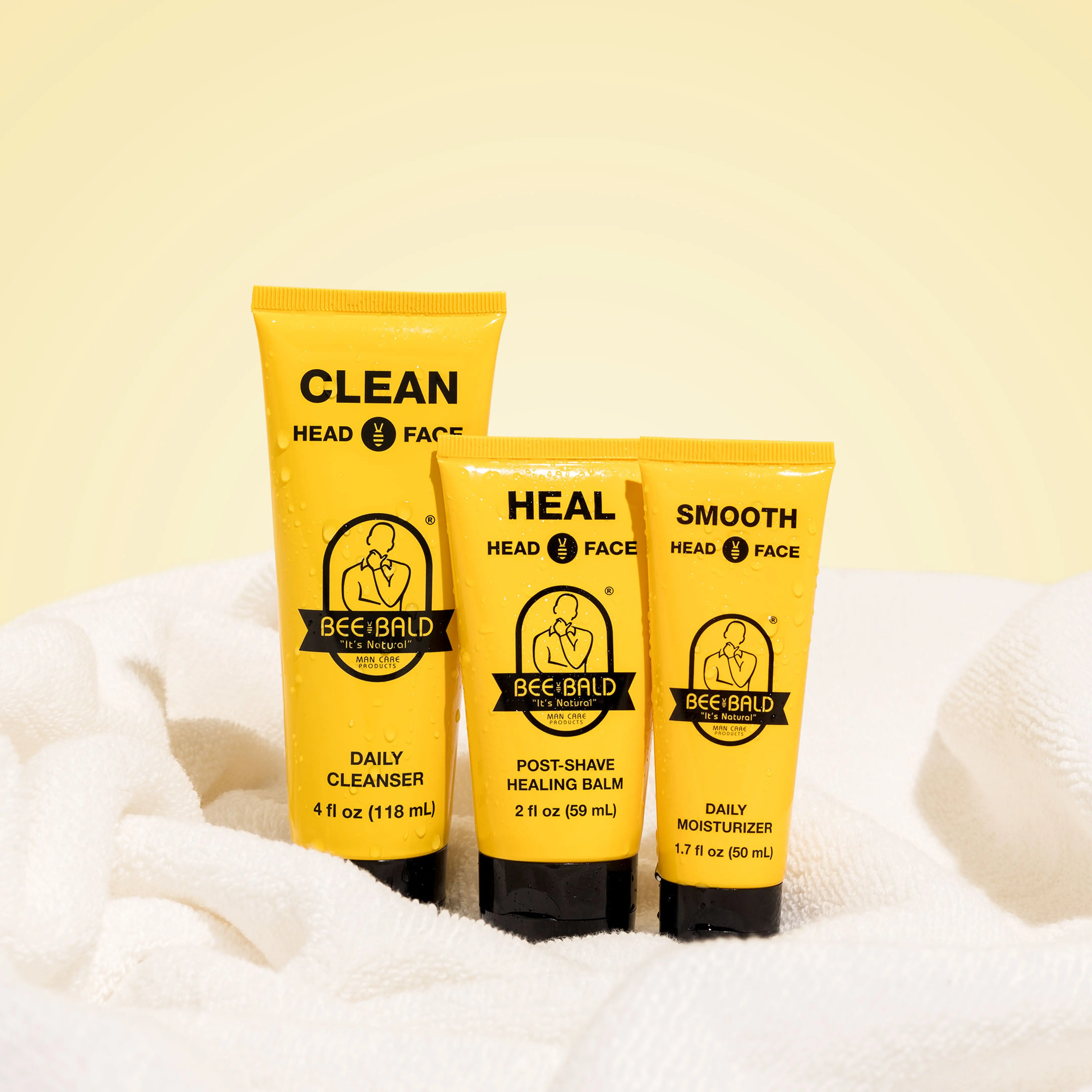 Three yellow Bee Bald skincare products on a white towel.