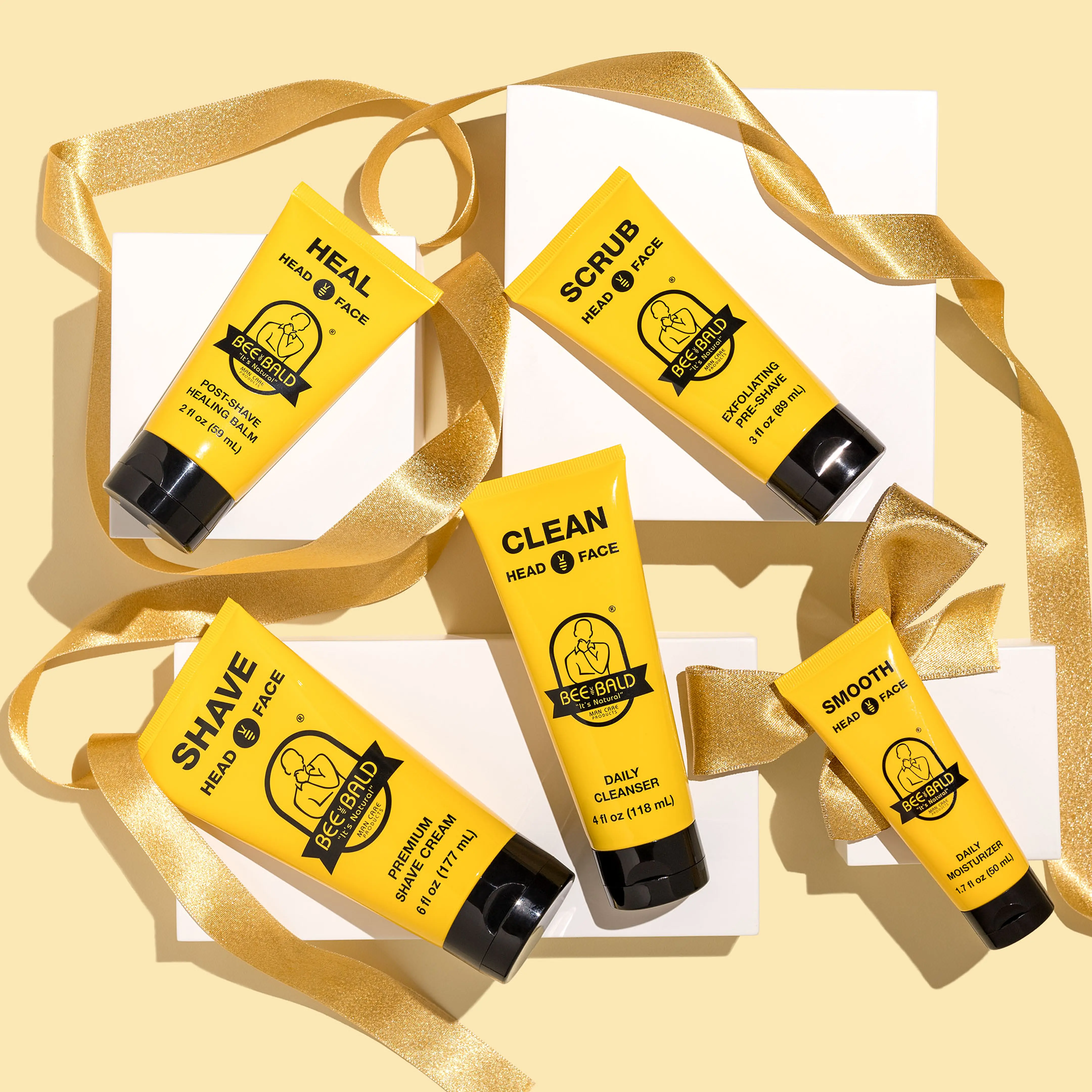 Yellow skincare products with black caps on a beige background, decorated with gold ribbons.