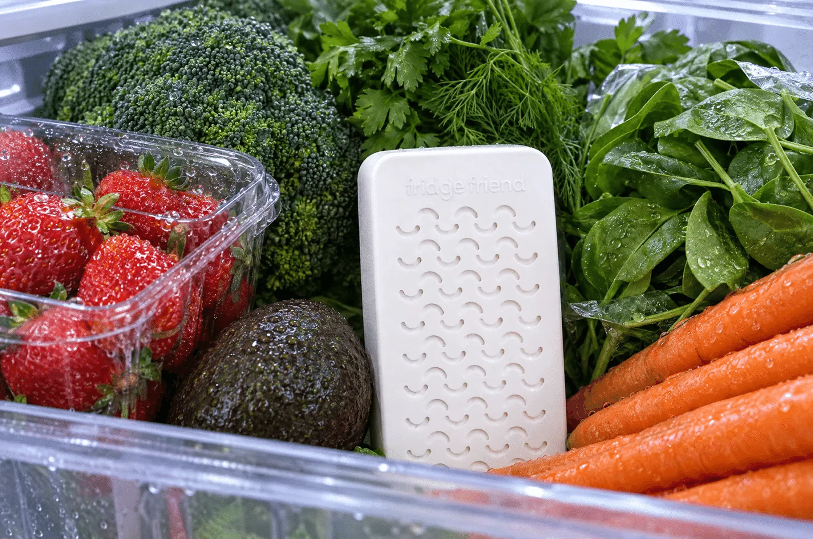 A refrigerator drawer filled with fresh produce and a white 'fridge friend' produce saver device.