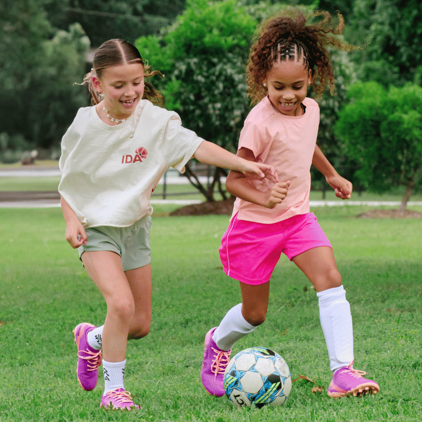 Two young girls smile while playing soccer together on a grassy field.