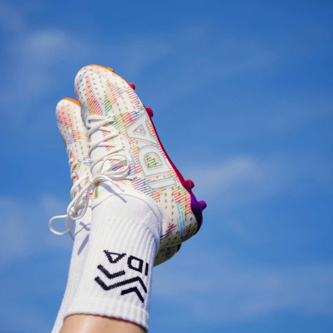 A pair of colorful, patterned soccer cleats held up against a bright blue sky.