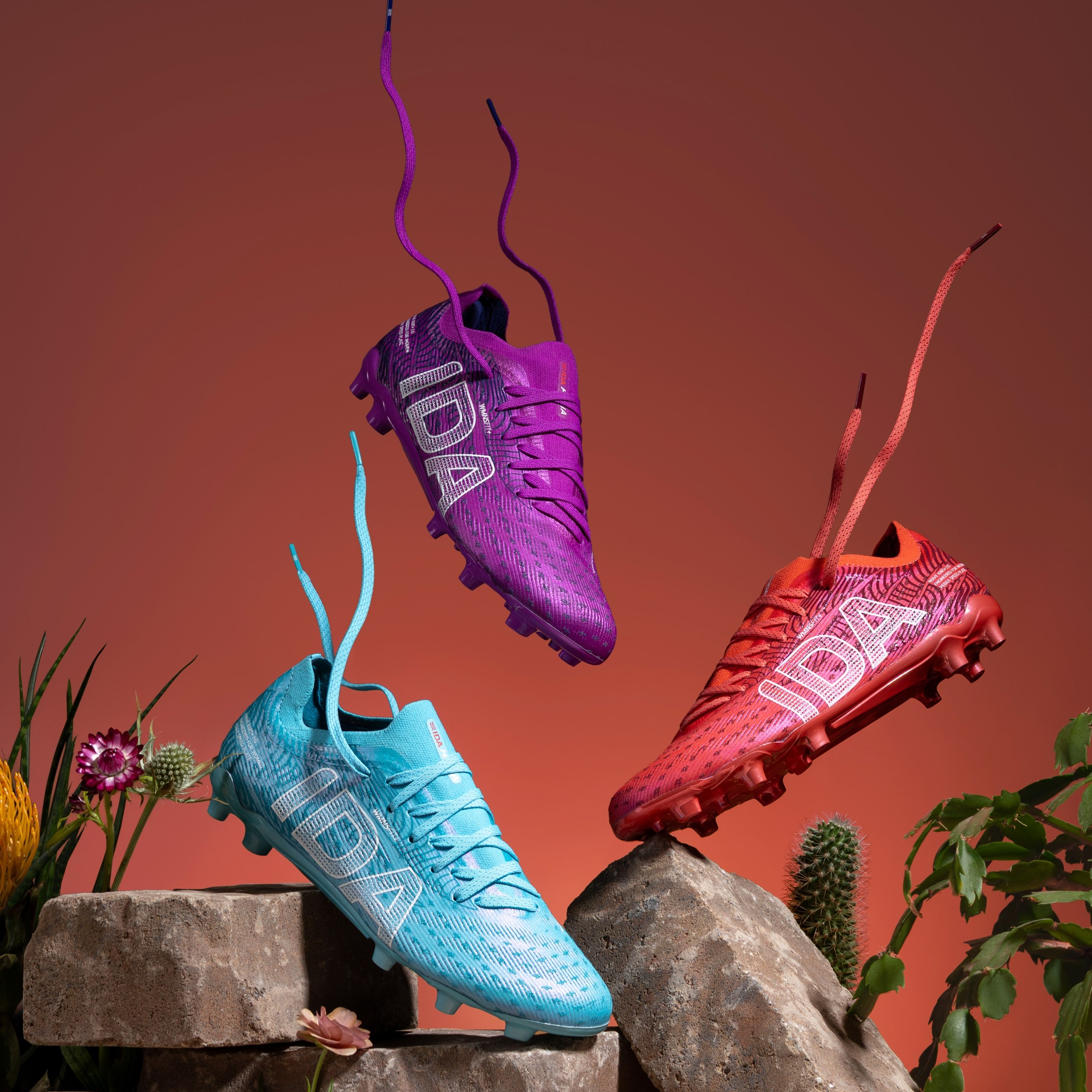 Three colorful soccer cleats suspended in air against an orange background.