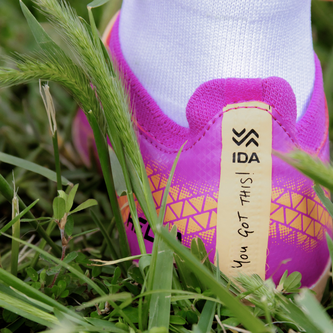 Close-up of the heel of a pink athletic shoe in grass with 'You Got This!' on the tab.