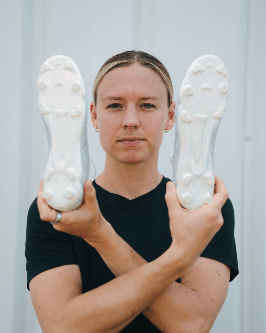 A person holds up the soles of two white soccer cleats in front of their face.