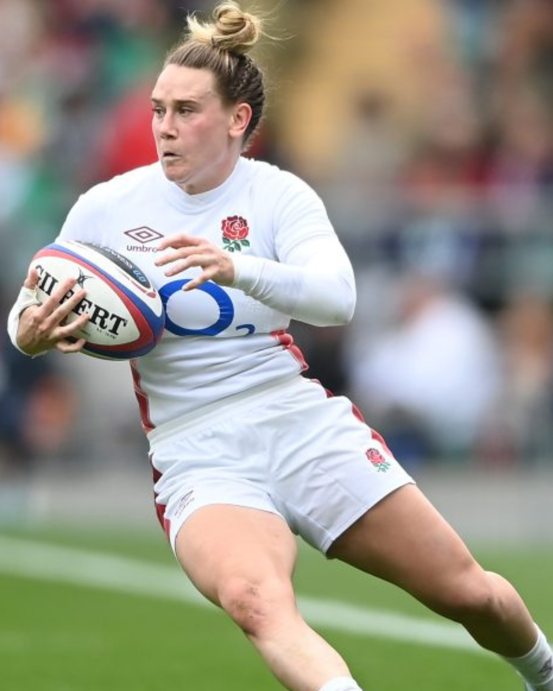 A rugby player in white jersey holding a rugby ball during a match.