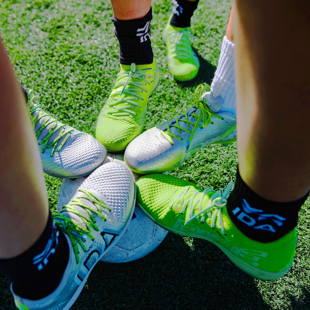 Five soccer shoes on a ball on green turf.