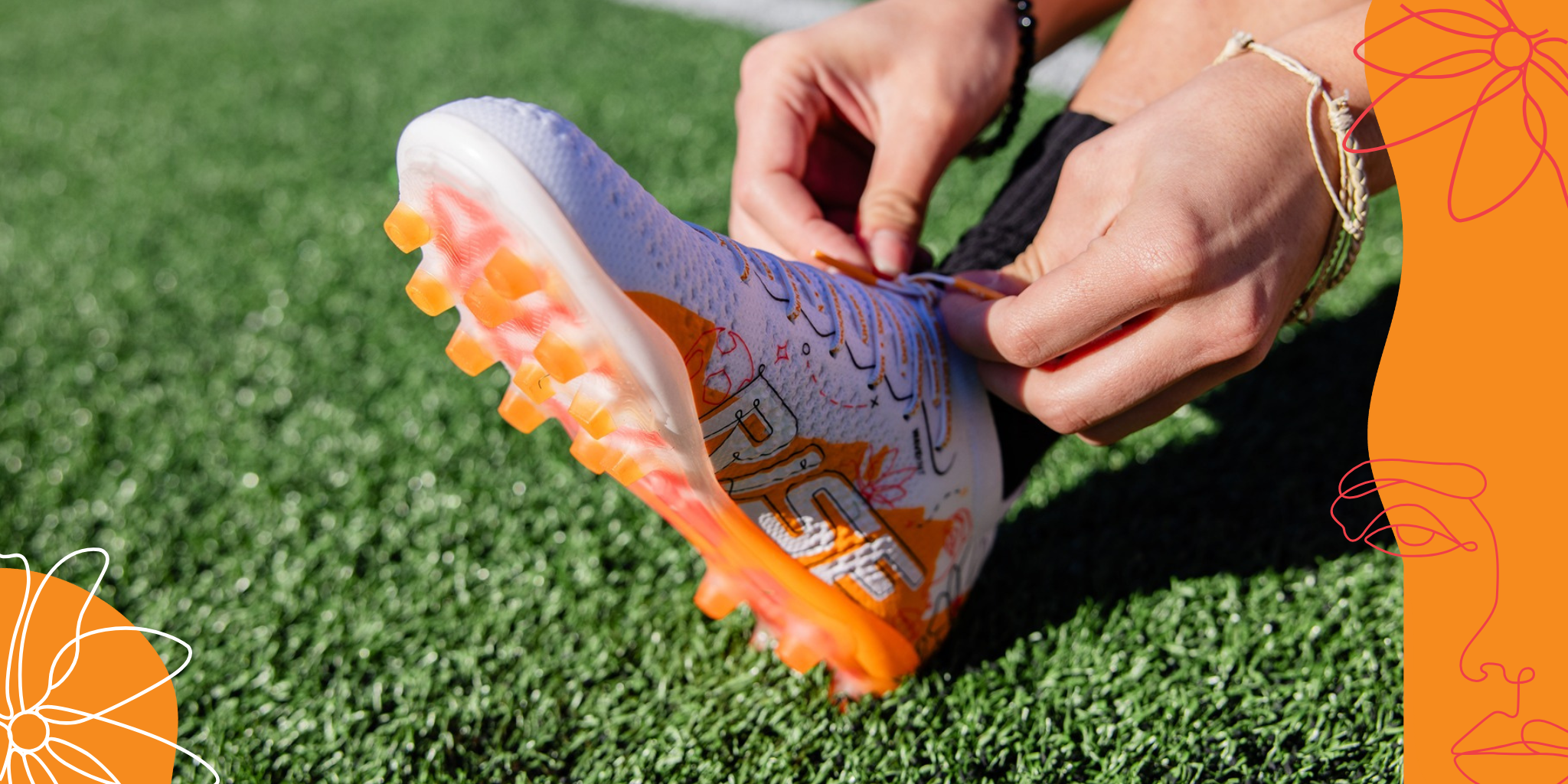 Person tying orange and white soccer cleats on green grass field.