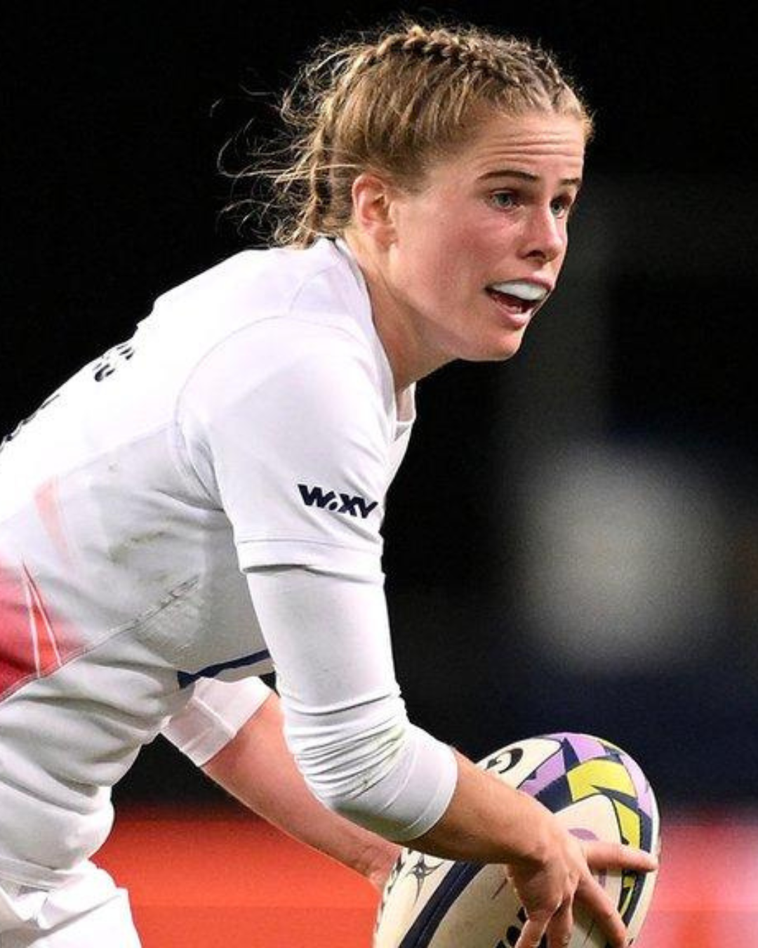 Rugby player in action holding a ball, wearing a white uniform with braided hair.