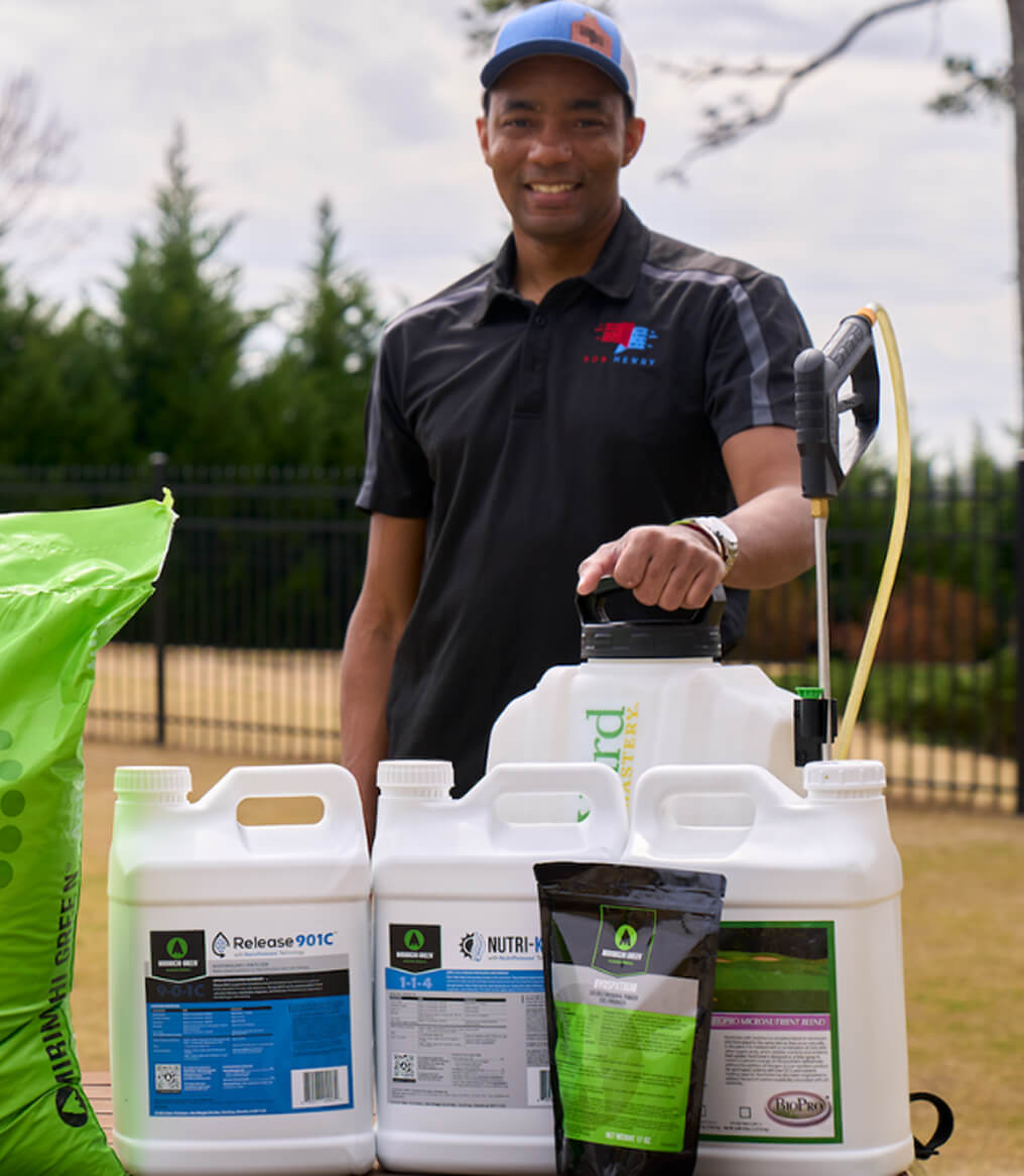 Person standing with lawn care products and a sprayer outdoors.