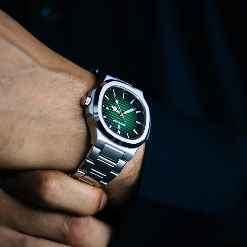 A wristwatch with a green face and silver band on a person's wrist.