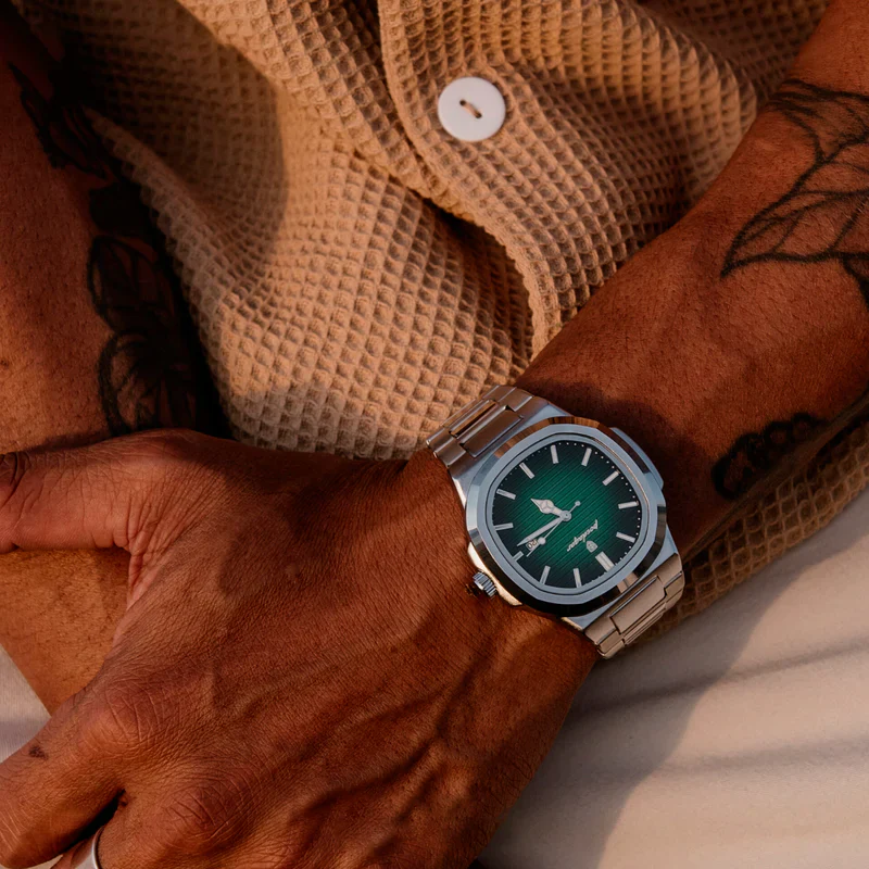 Person wearing a silver watch with a green face, resting on a beige textured fabric.