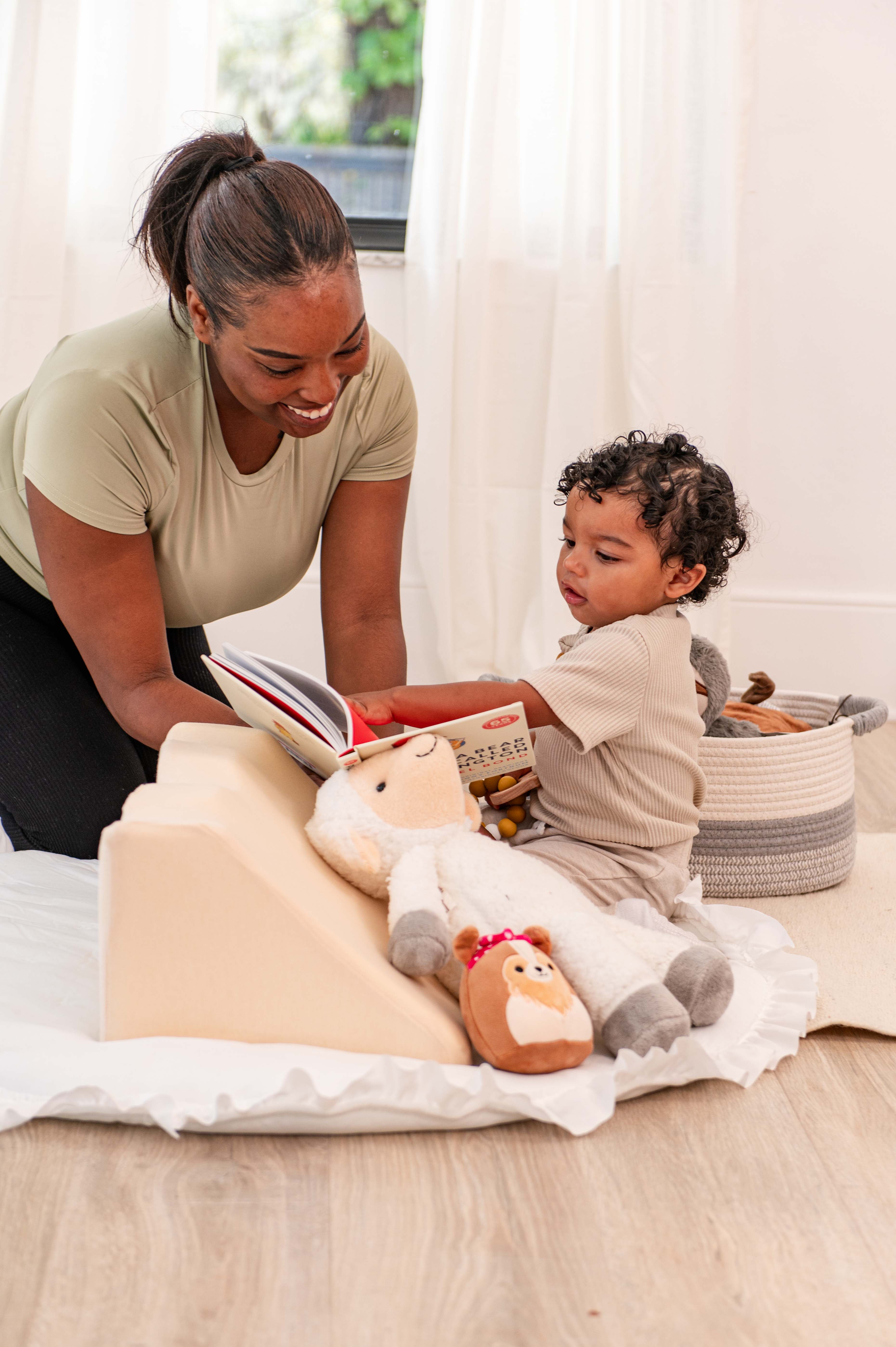 Woman reading a book to a child on the floor with toys around.