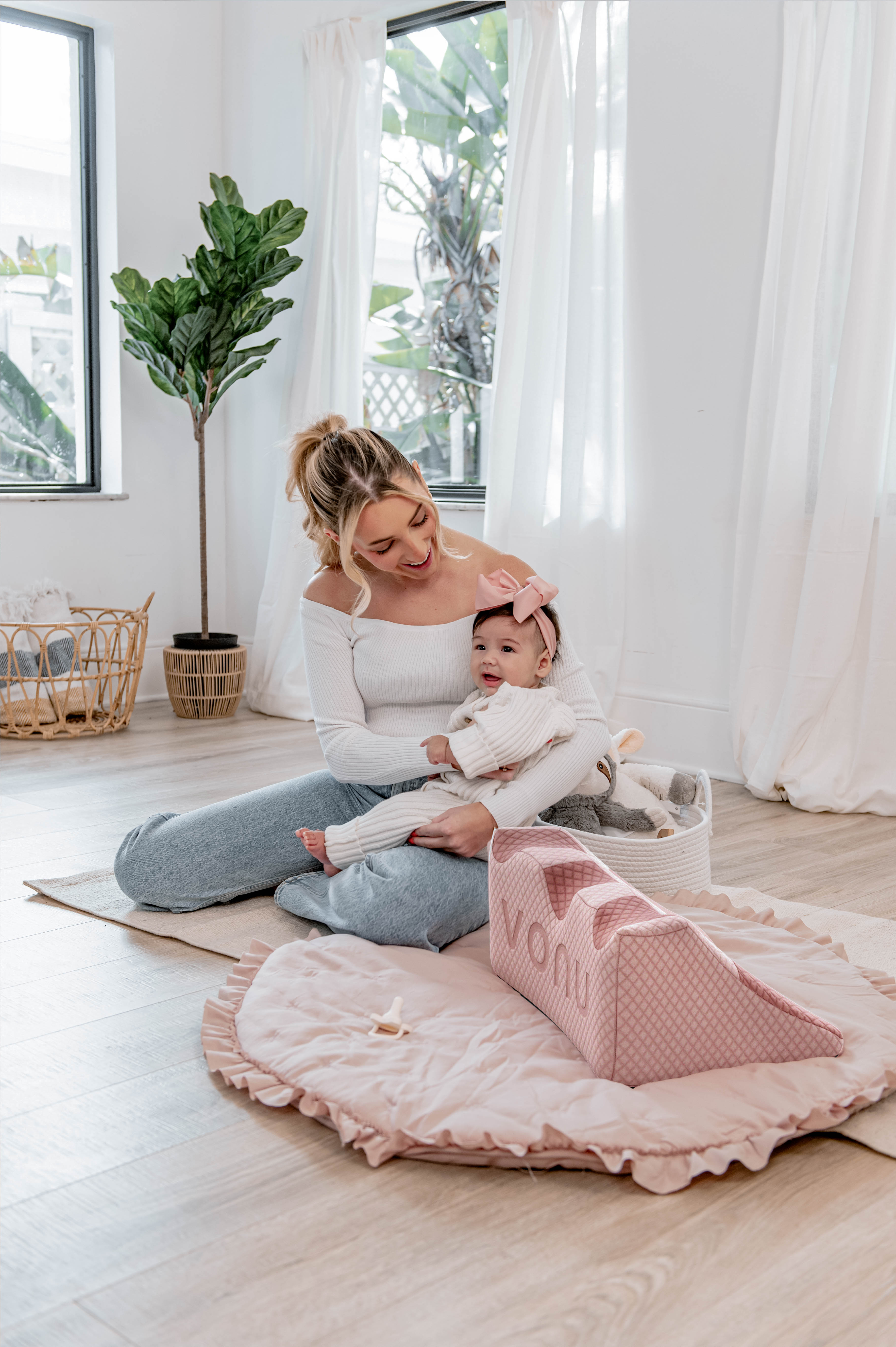 Woman smiling at a baby with a pink bow in a cozy, light-filled room.