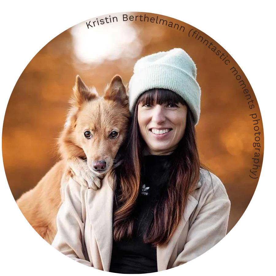 Woman in beanie with dog against autumn backdrop.