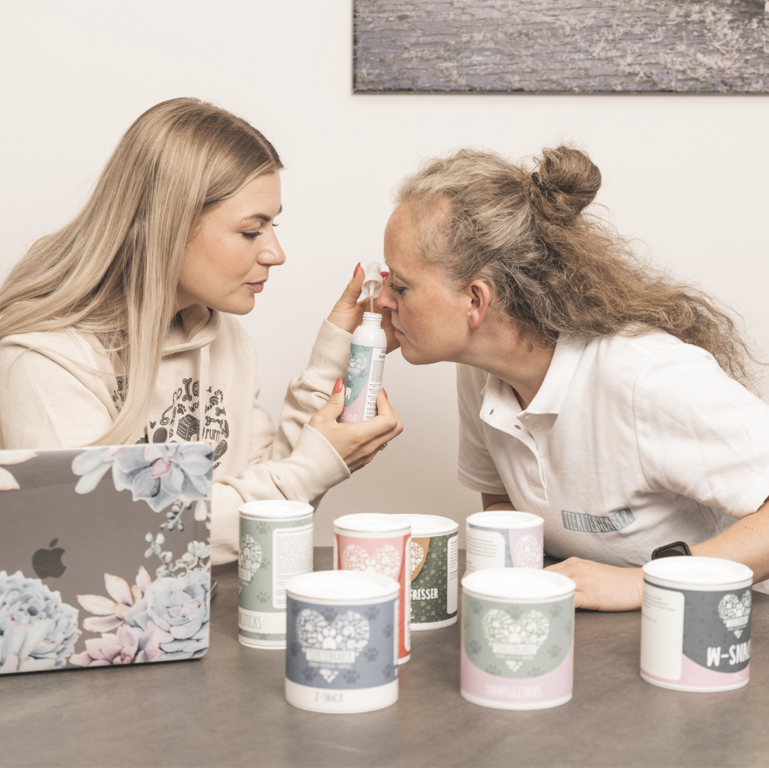 Two individuals discussing beauty or wellness products at a table with a laptop and various containers.