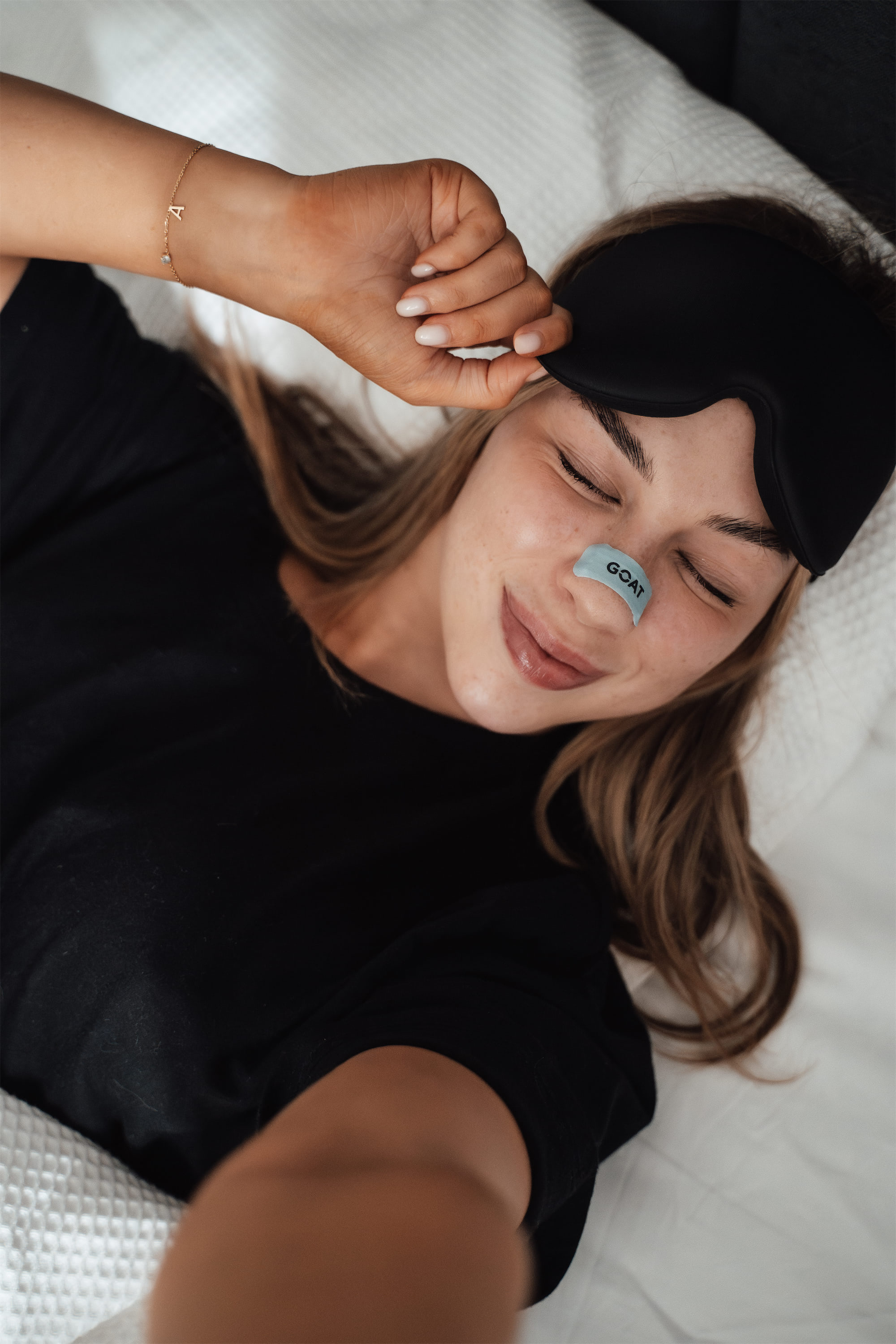 Person lying in bed with eye mask and nasal strip.