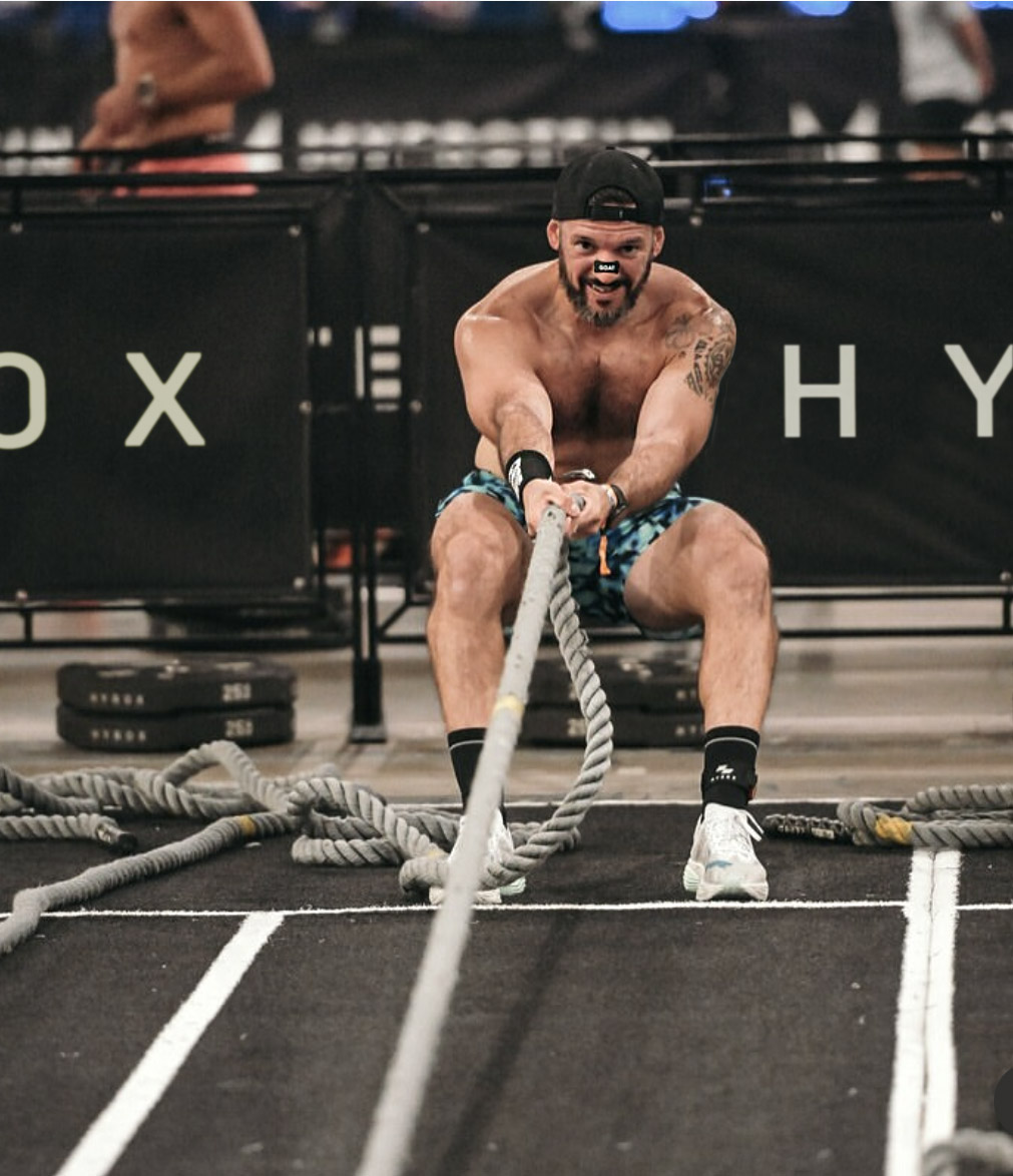 Man in a cap pulling a thick rope vigorously in a gym setting.