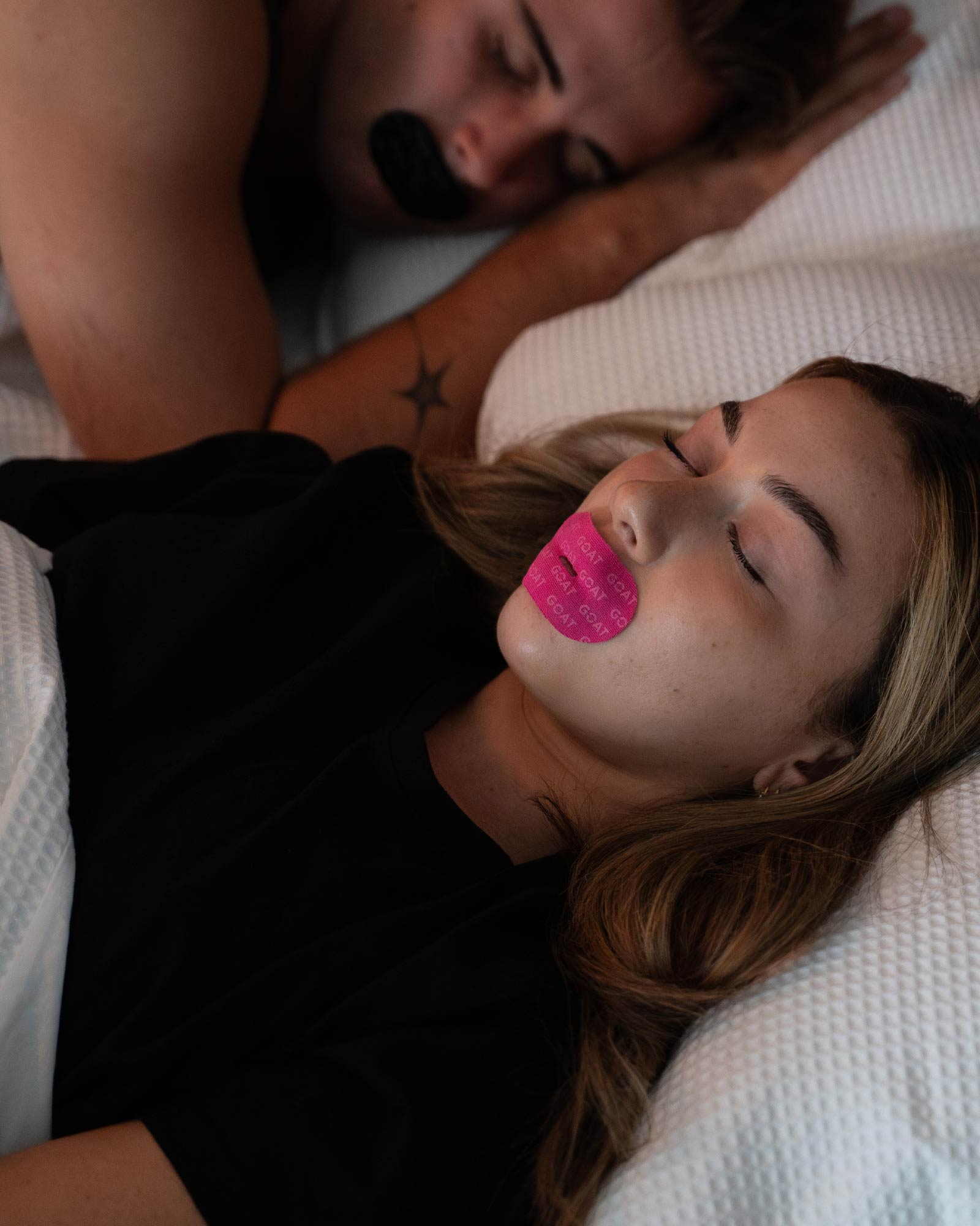 Two people sleeping with tape over their mouths.