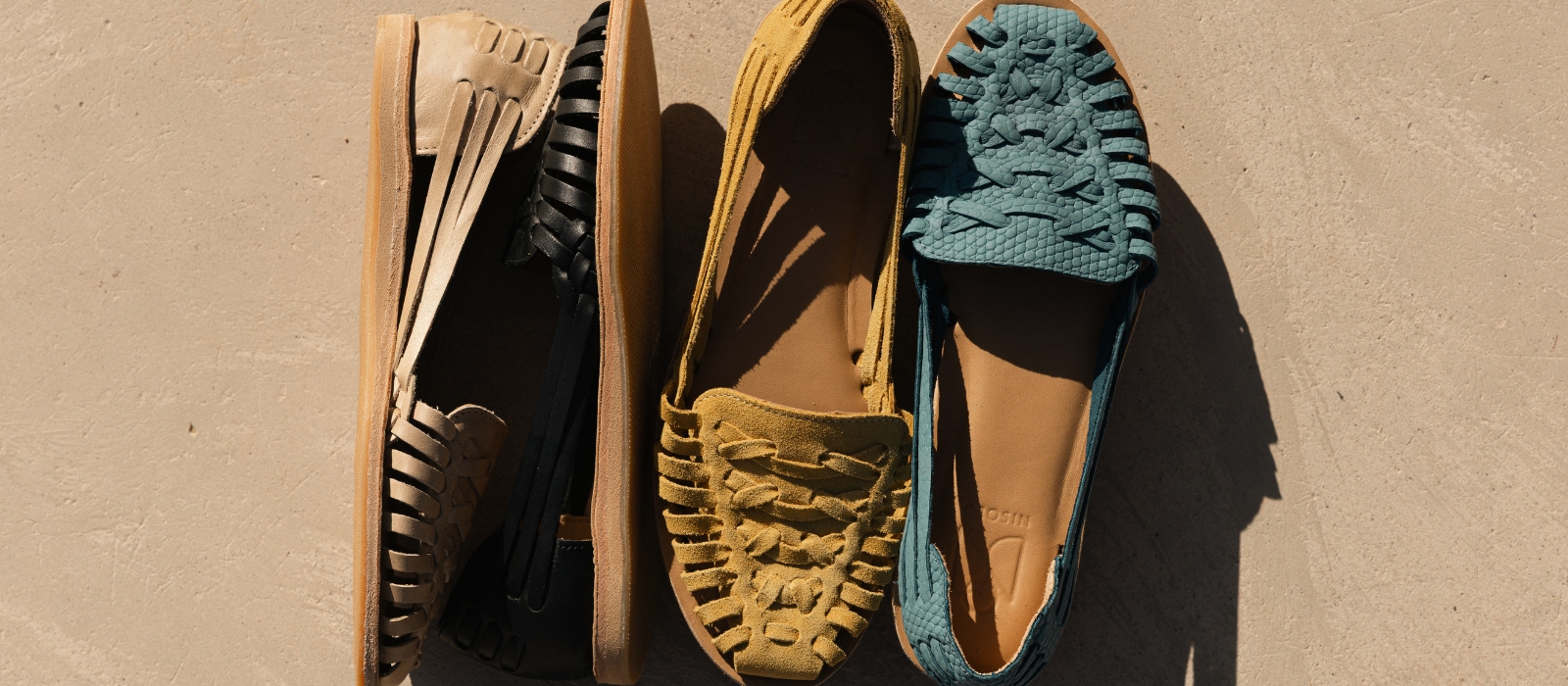 A top-down view of four colorful woven leather loafers arranged side by side on a textured surface.