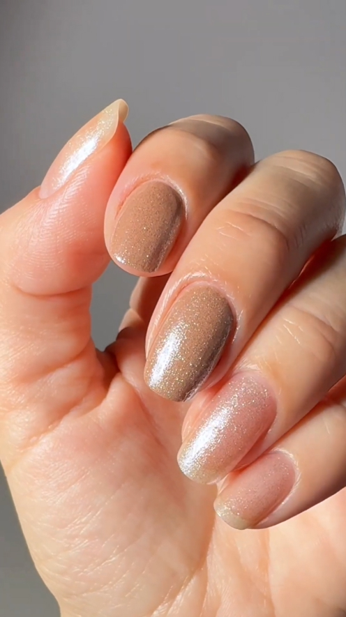 A close-up of a hand with a manicure featuring different shades of shimmery, neutral-colored nail polish.
