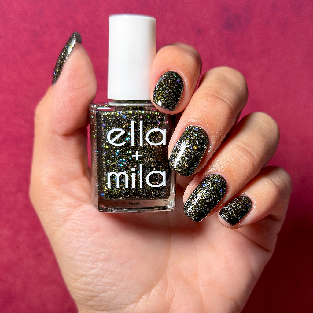 A hand holds a bottle of black glitter nail polish with a matching manicure against a pink background.