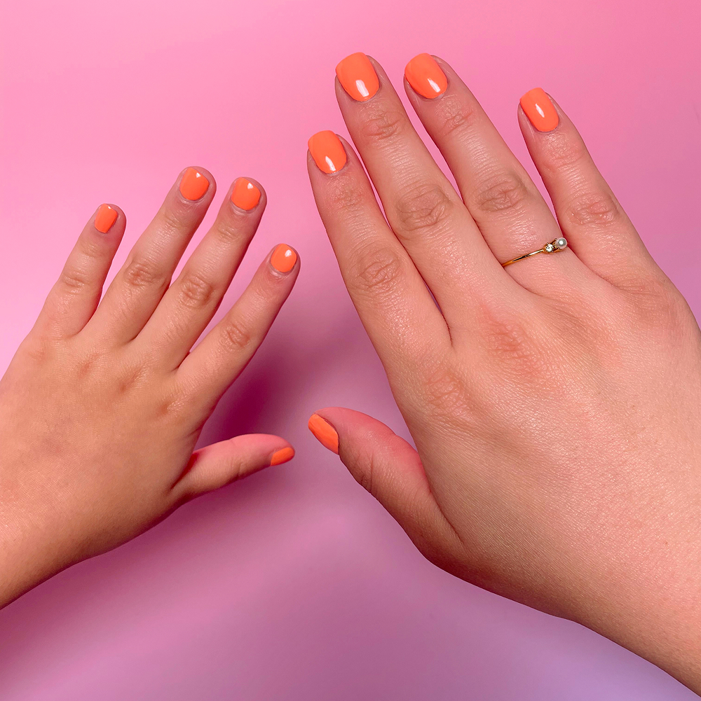 An adult's hand and a child's hand with matching orange manicures on a pink background.