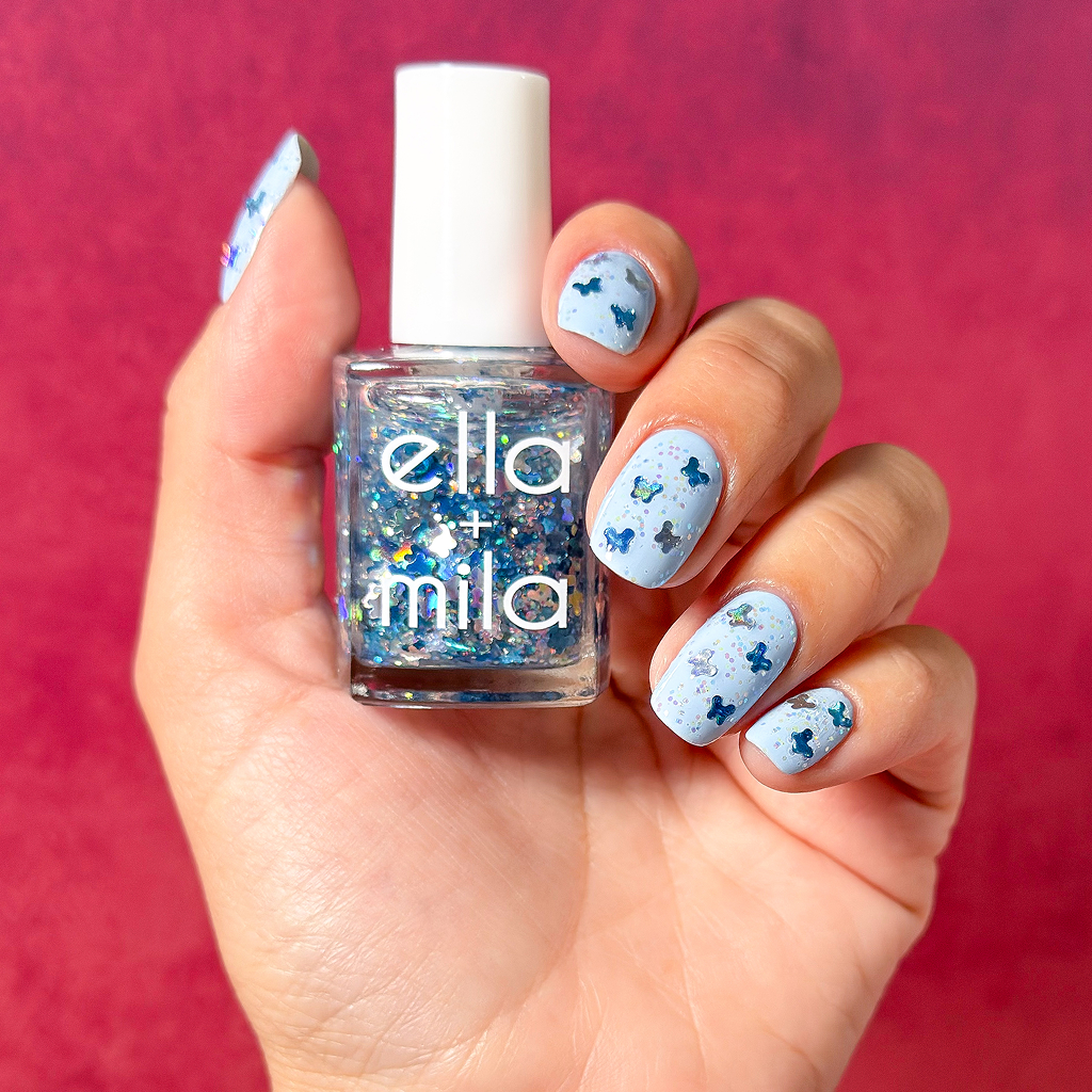 A hand with a light blue manicure featuring glittery butterflies holds a bottle of matching nail polish.