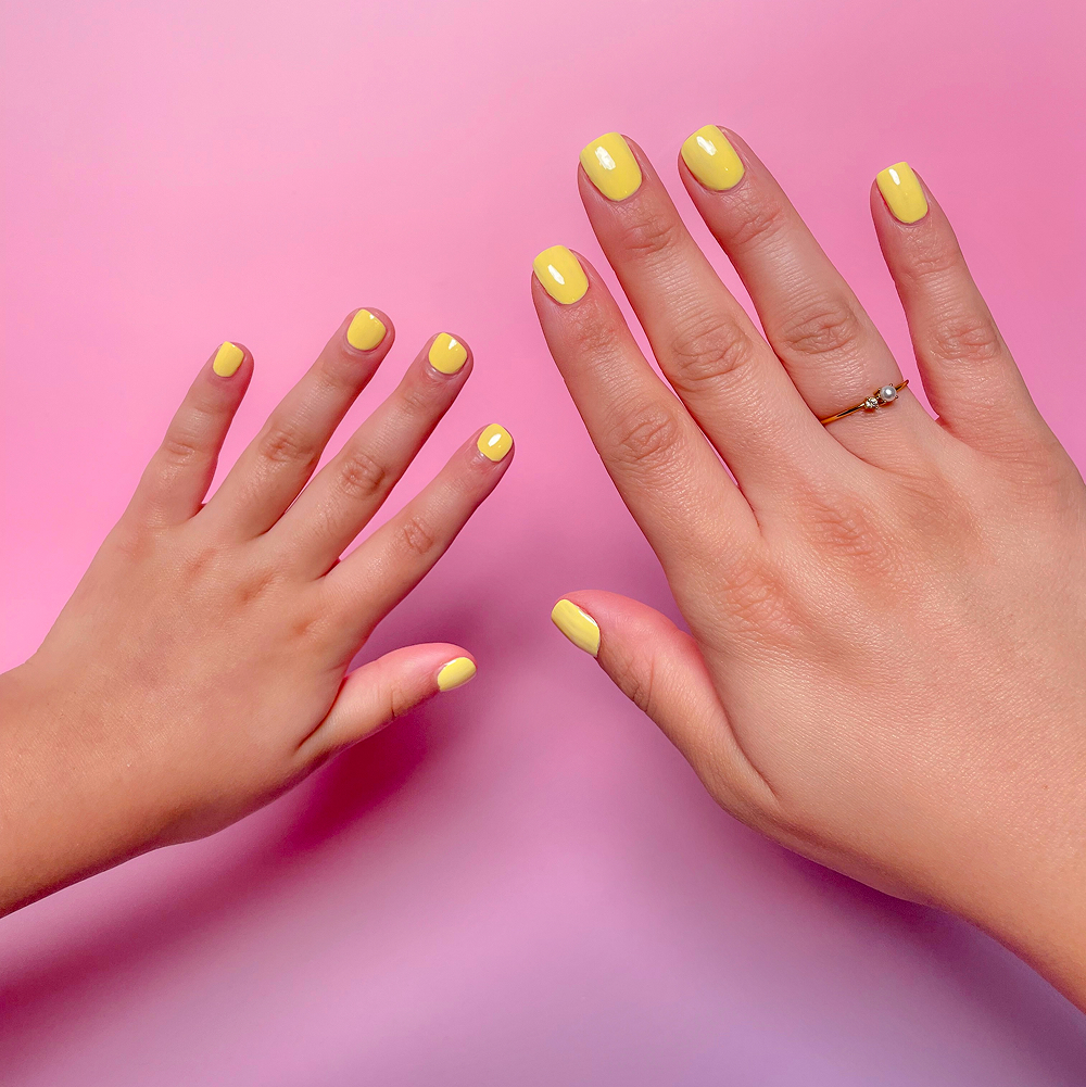 An adult's hand and a child's hand with matching yellow nail polish against a pink background.