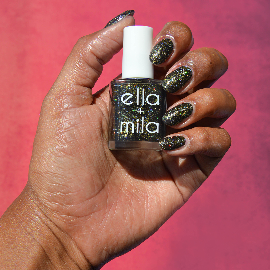 A hand with a black and gold glitter manicure holding a matching bottle of nail polish.