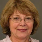 A woman with glasses and short hair smiling at the camera.