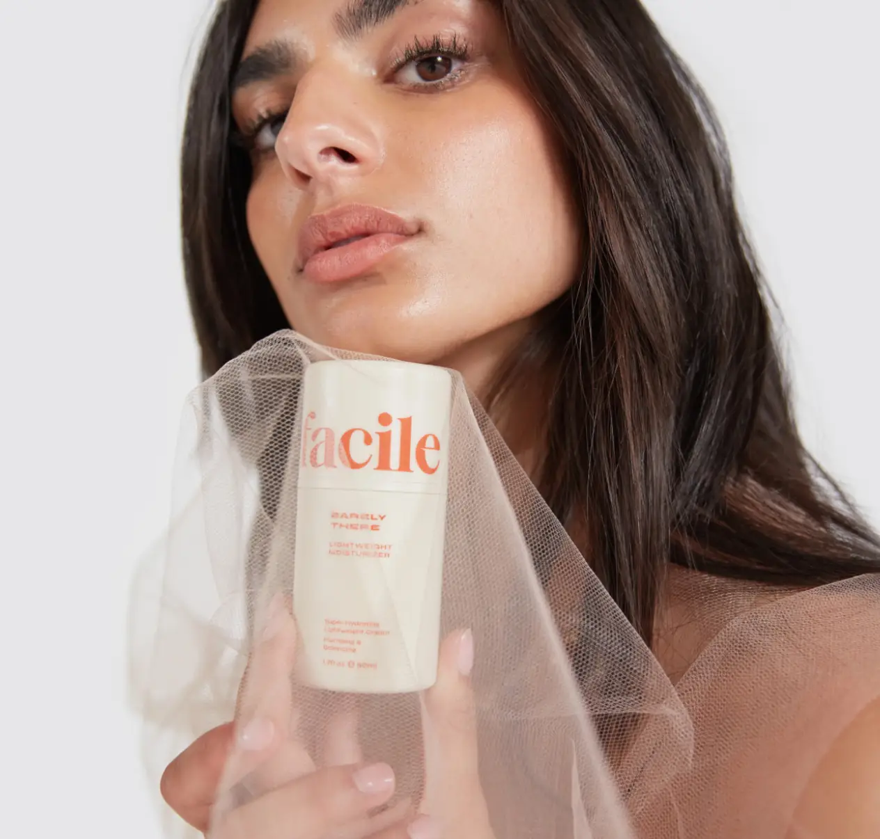 Person holding a skincare product with a sheer fabric overlay.