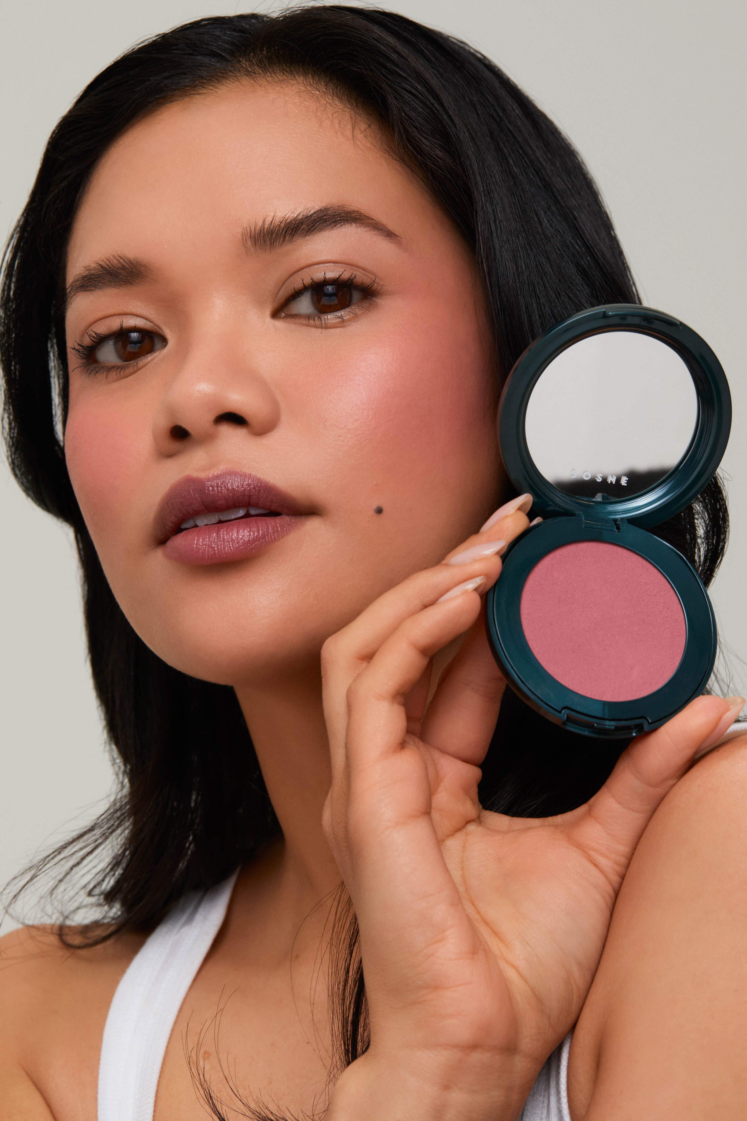 Person holding a compact with pink blush, close-up view.