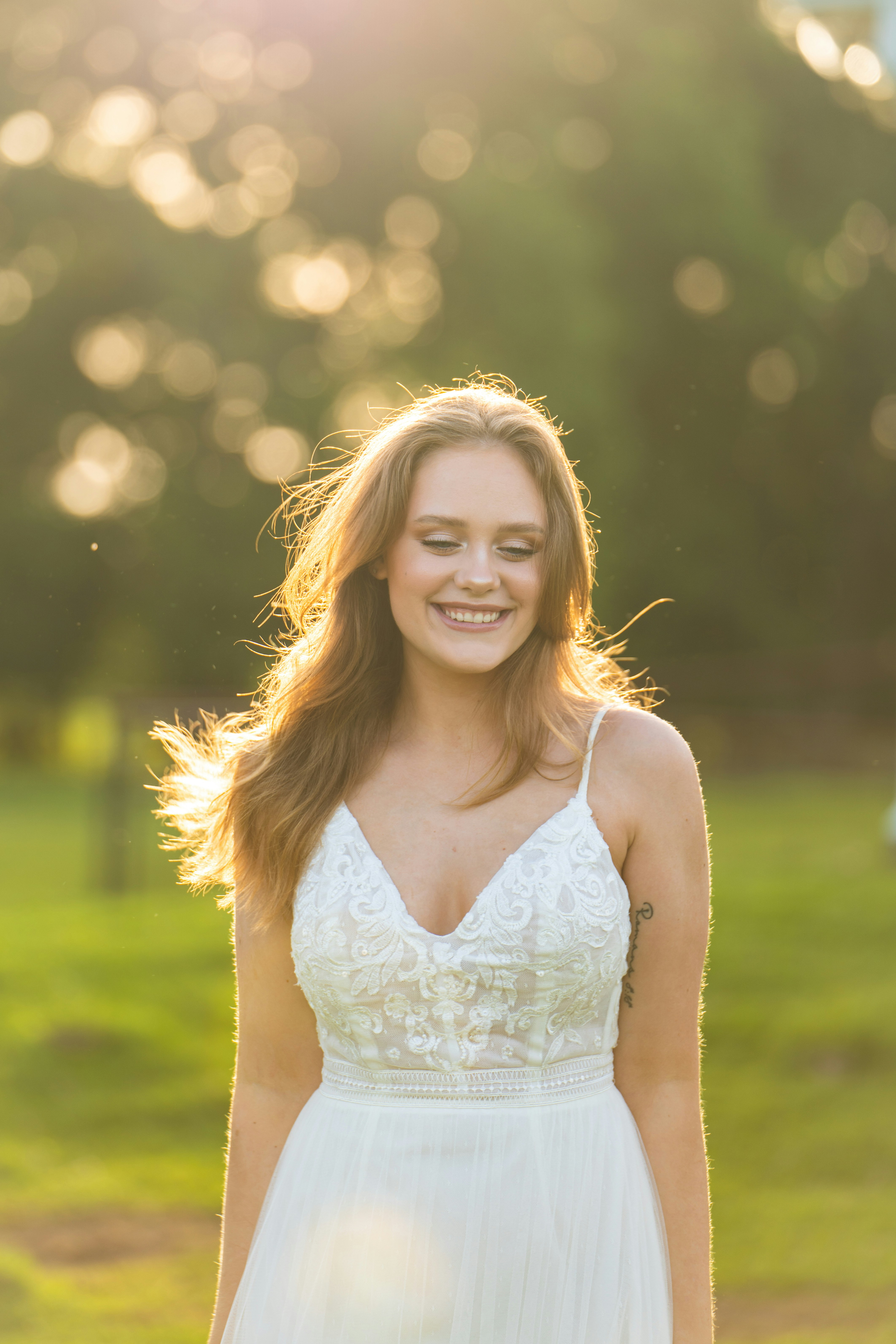 Smiling woman in a white dress standing outdoors with sunlight behind her.