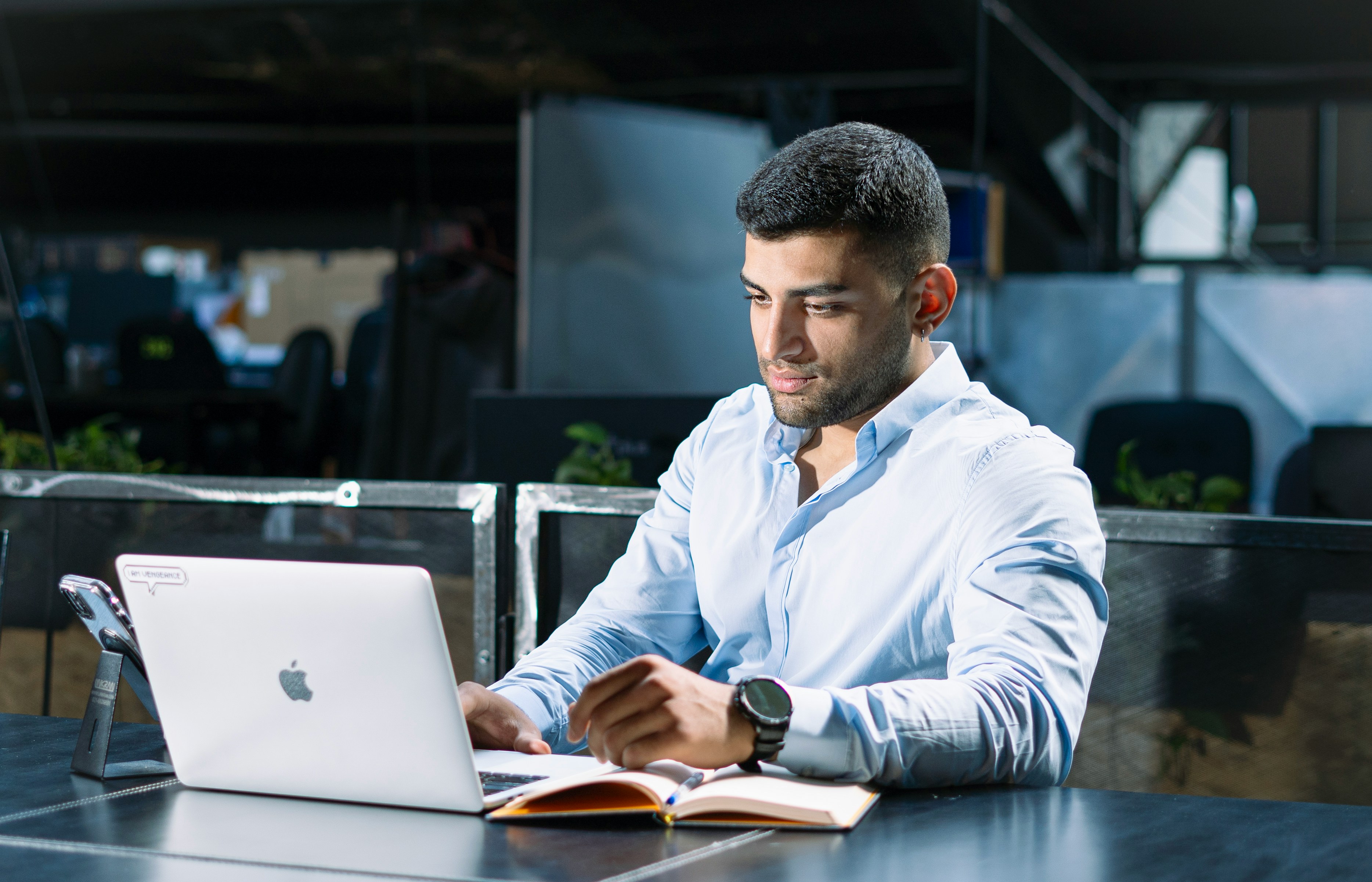 Man in a blue shirt working on a laptop at a desk.